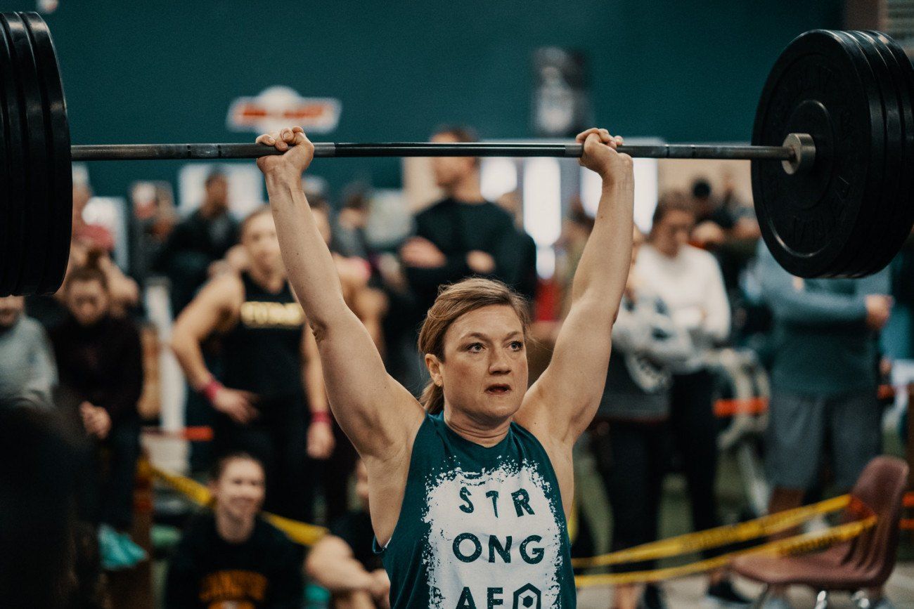 Woman lifting a barbell overhead at a competition, wearing a 