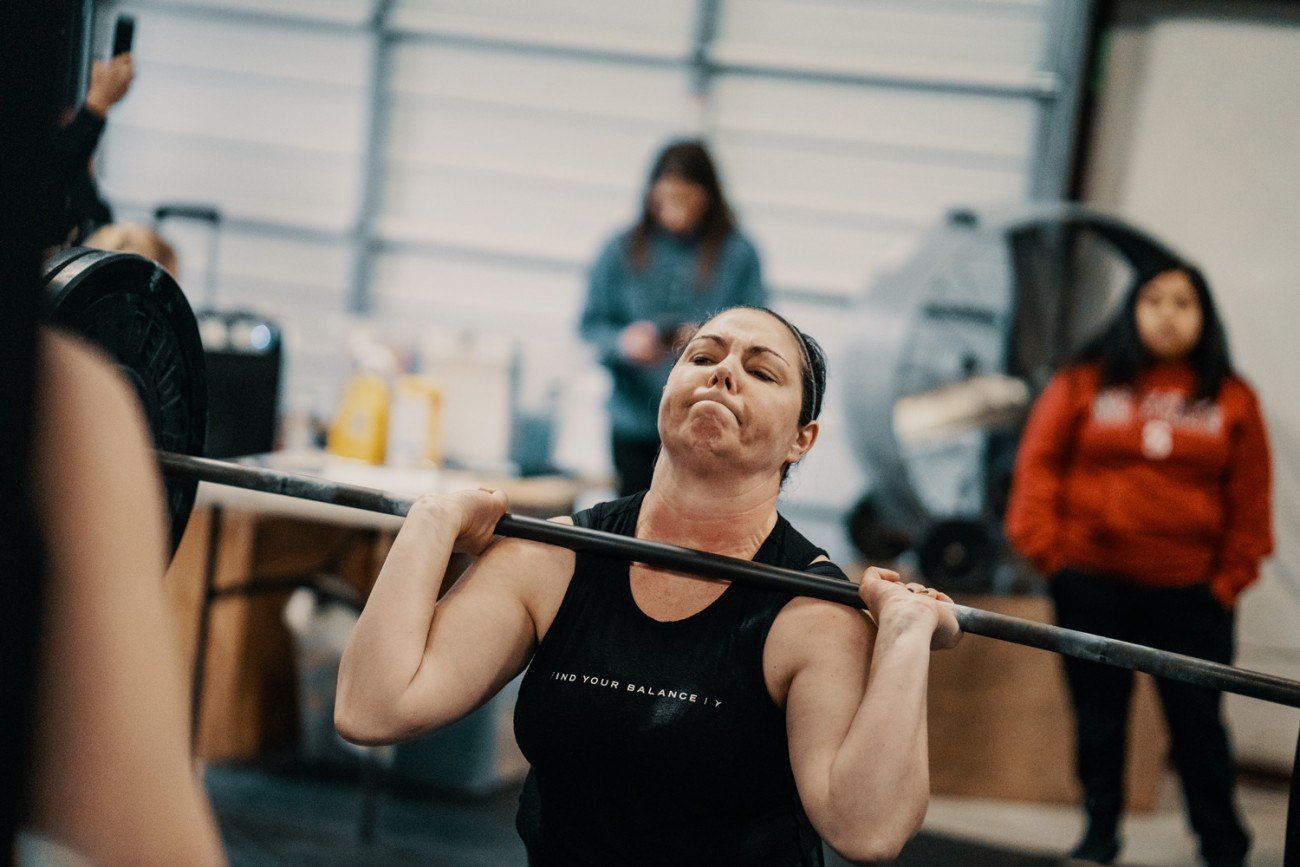 Woman straining to lift a barbell overhead in a gym, face contorted with effort.