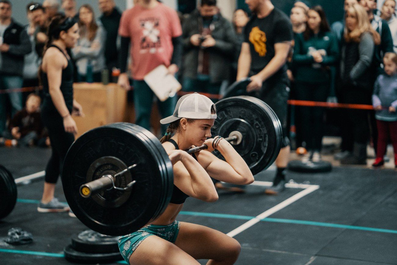Woman in a hat performing a front squat with a barbell in a competition setting.