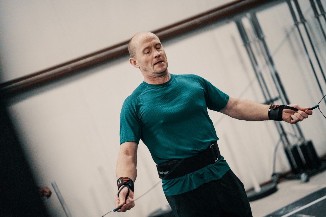 Man in turquoise shirt skipping rope in a gym, with focus on the exercise.