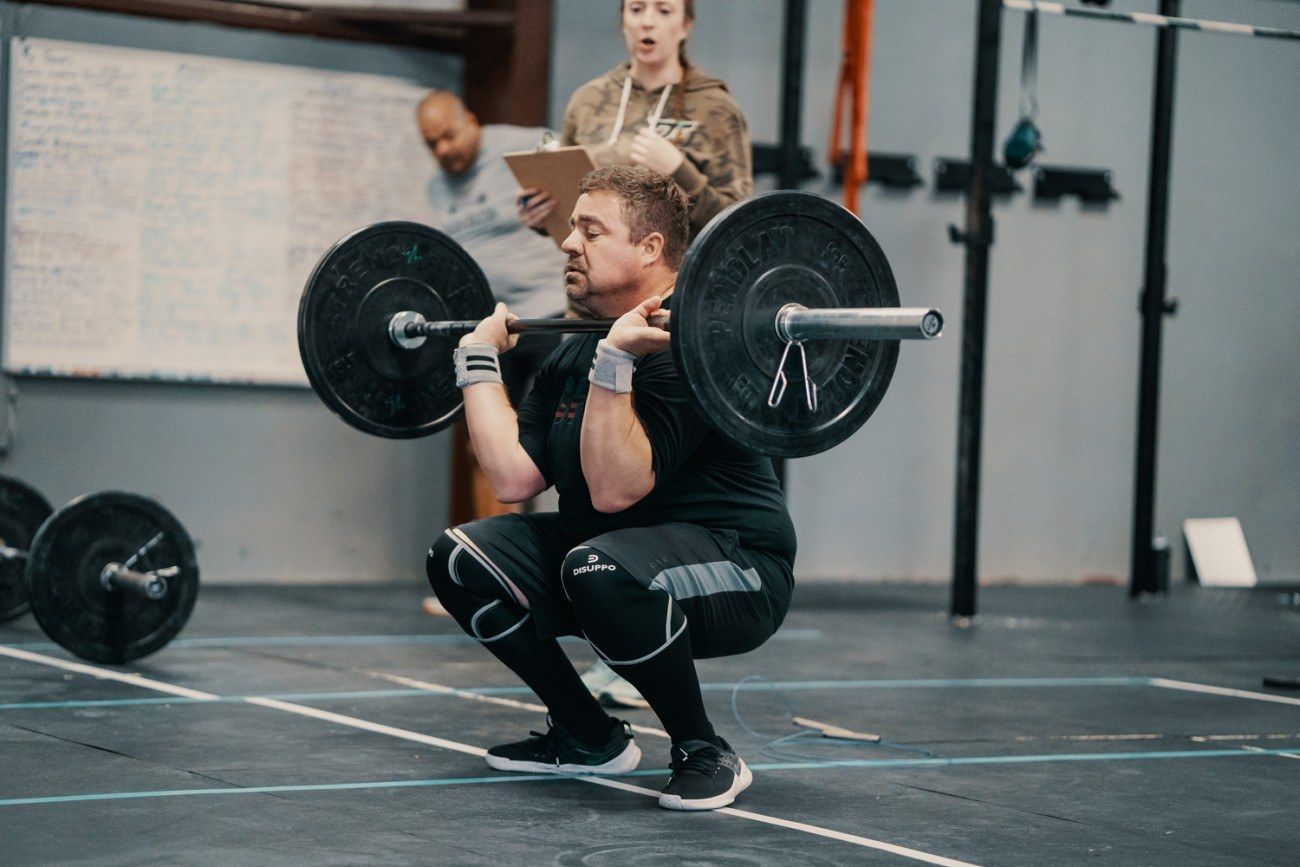 Weightlifter in black holding barbell, performing a front squat in a gym setting.