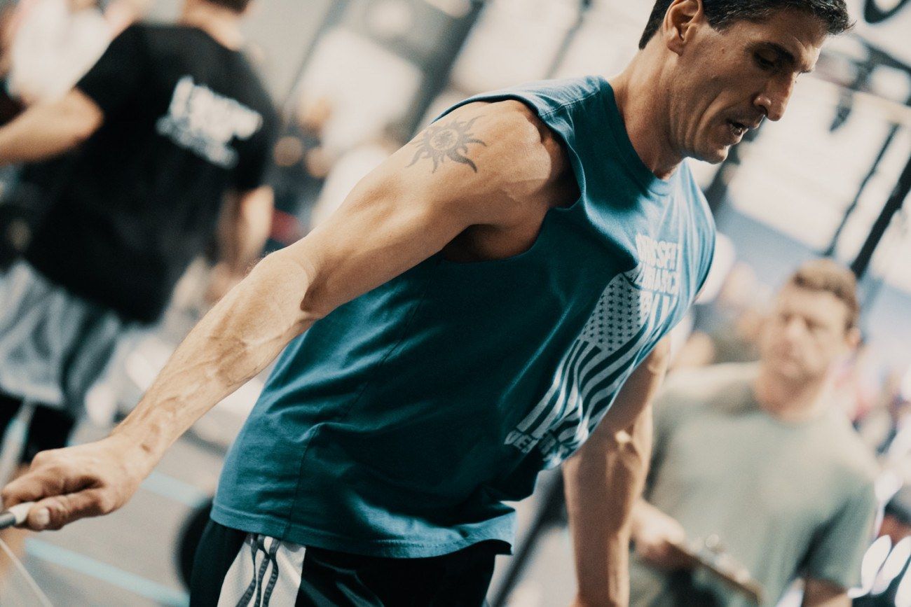 Man skipping rope in a gym, wearing a blue sleeveless shirt.