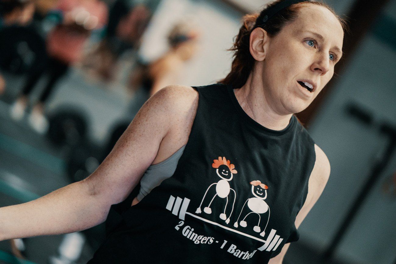 Woman in gym, wearing a tank top with cartoon figures, breathing heavily, blurred background.