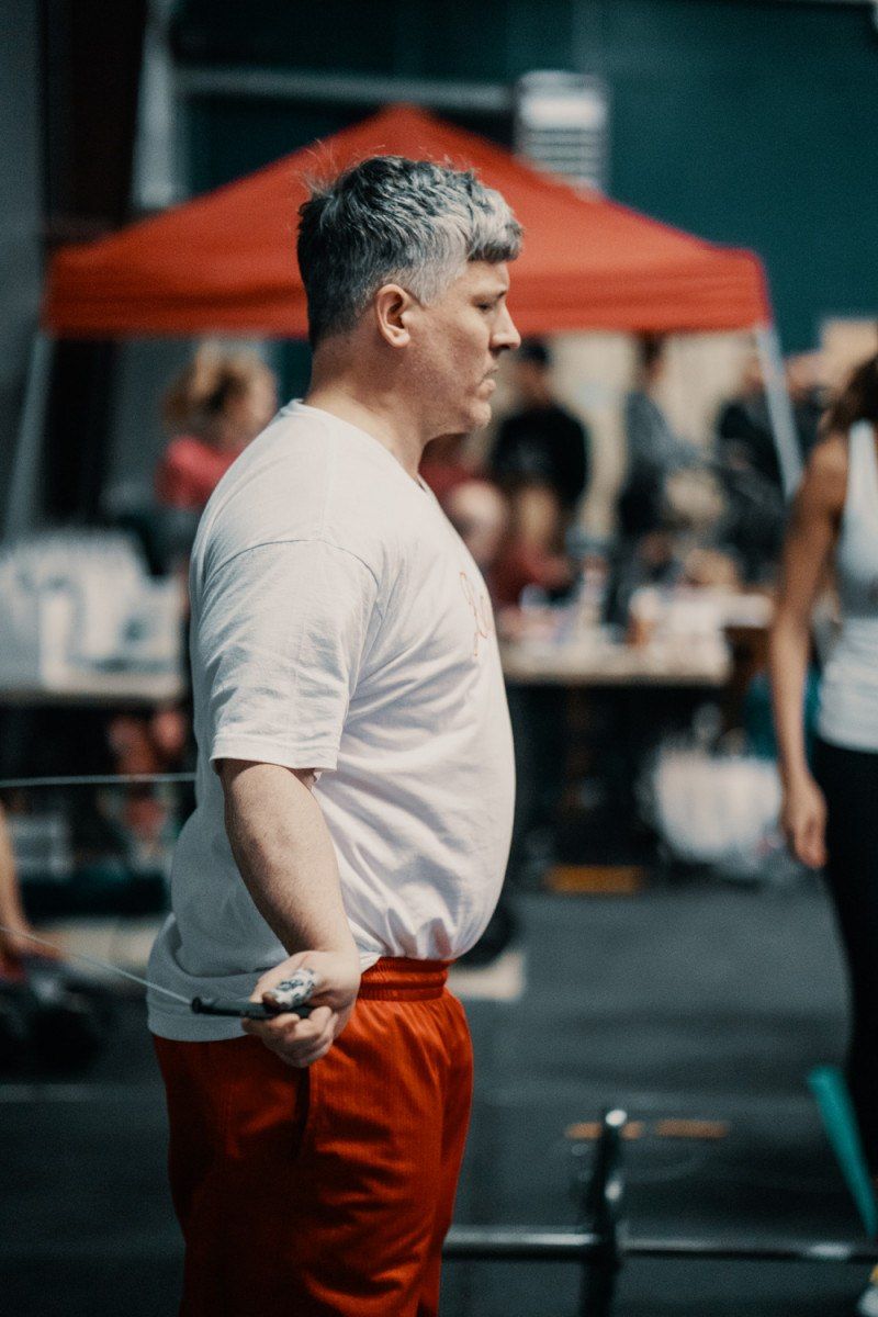 Man in red pants and white shirt, holding a jump rope in a gym setting.