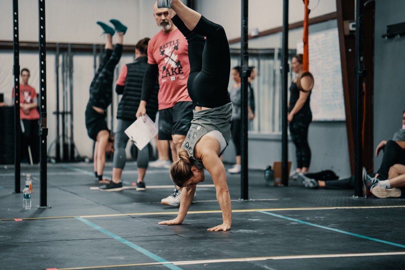People doing handstands in a gym. A coach watches with clipboard in hand.
