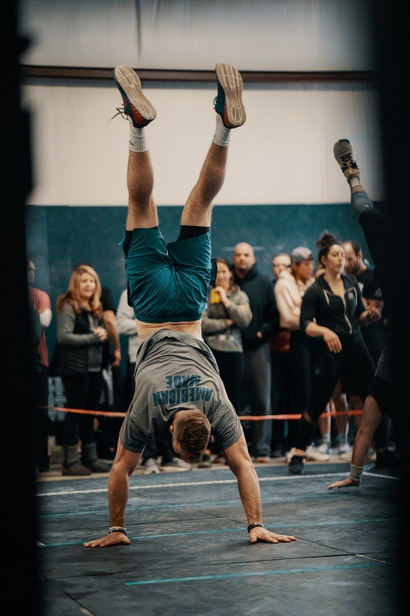 Athlete doing a handstand in a gymnasium, with spectators in the background.