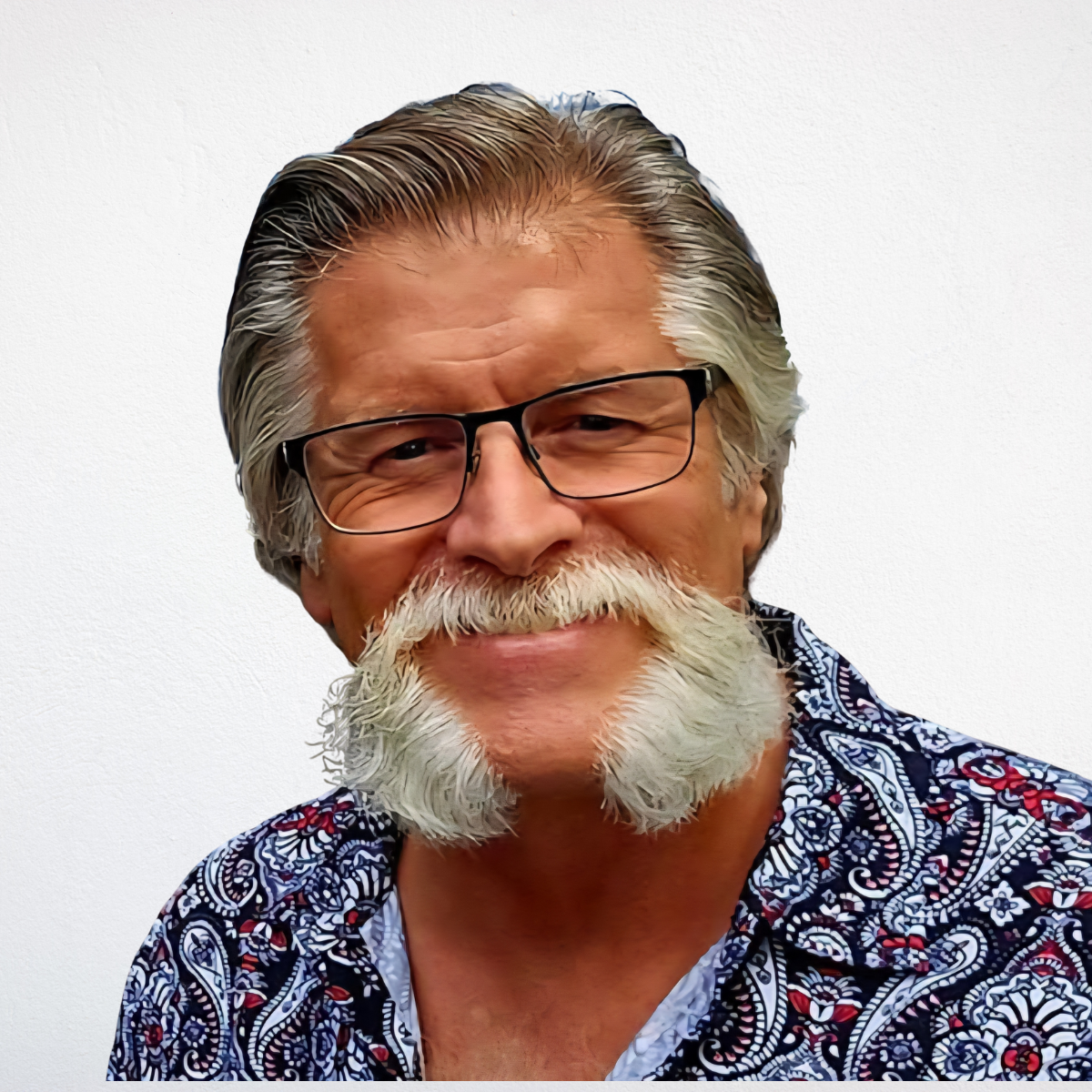 Man with graying hair, mustache and mutton chops, wearing glasses and patterned shirt.