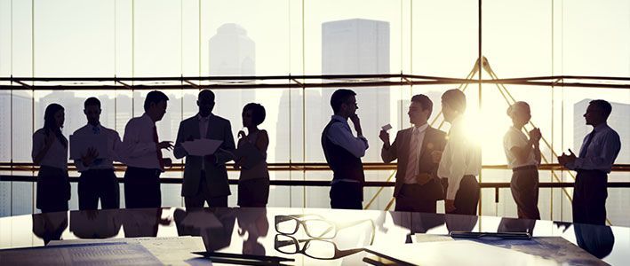 A group of business people are standing around a table in front of a window.