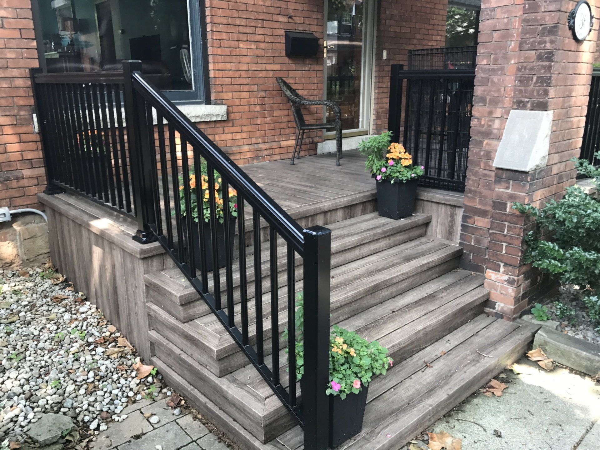 A wooden deck with stairs and a black railing in front of a brick house.