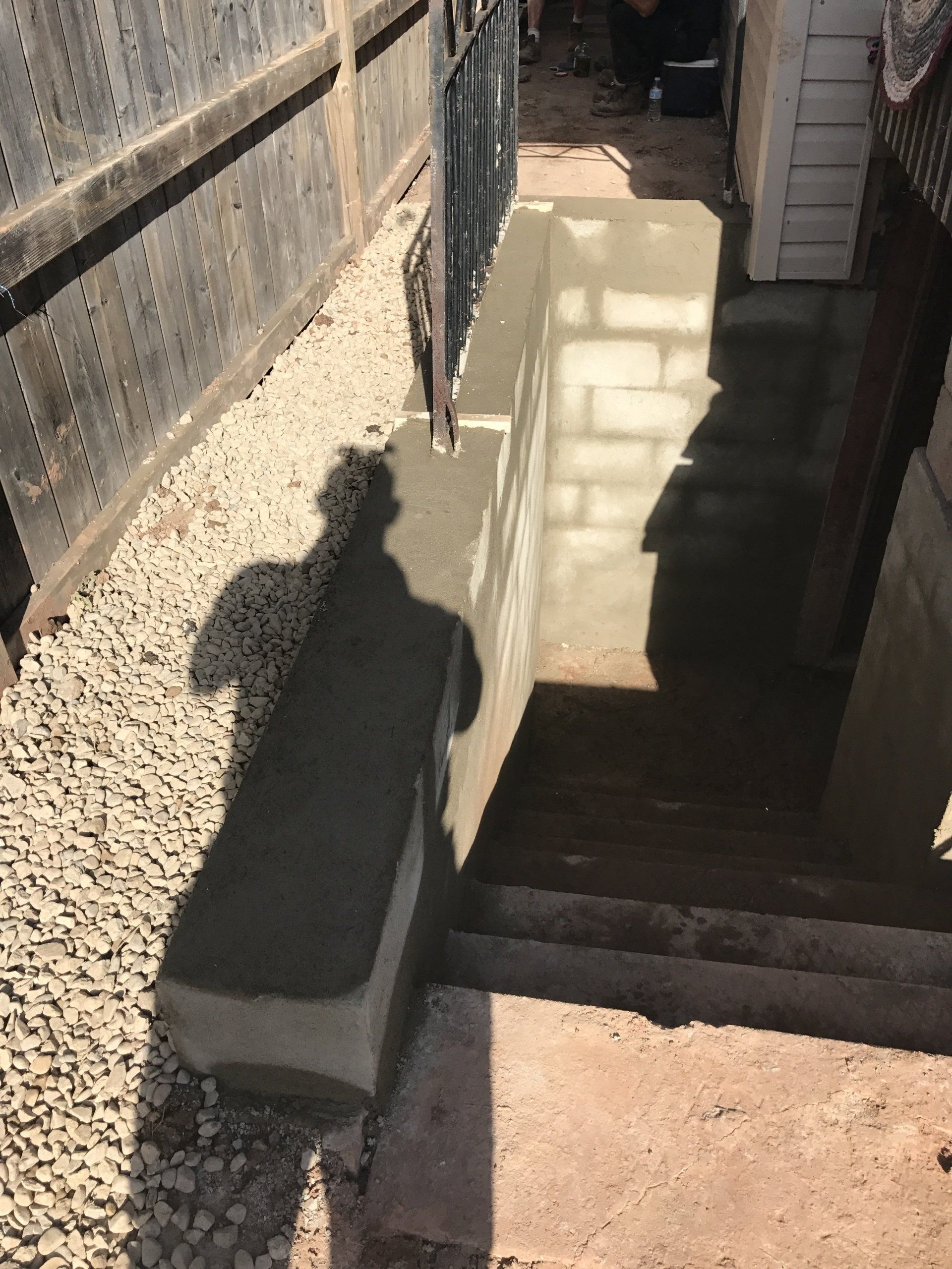 A shadow of a person is cast on a concrete wall next to stairs.