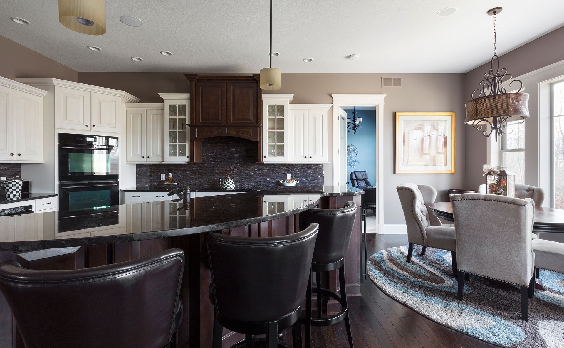 A kitchen and dining room in a house with white cabinets and black counter tops.