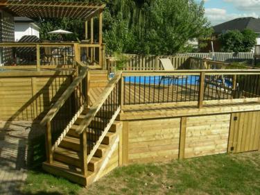 A wooden deck with stairs and a pool in the background