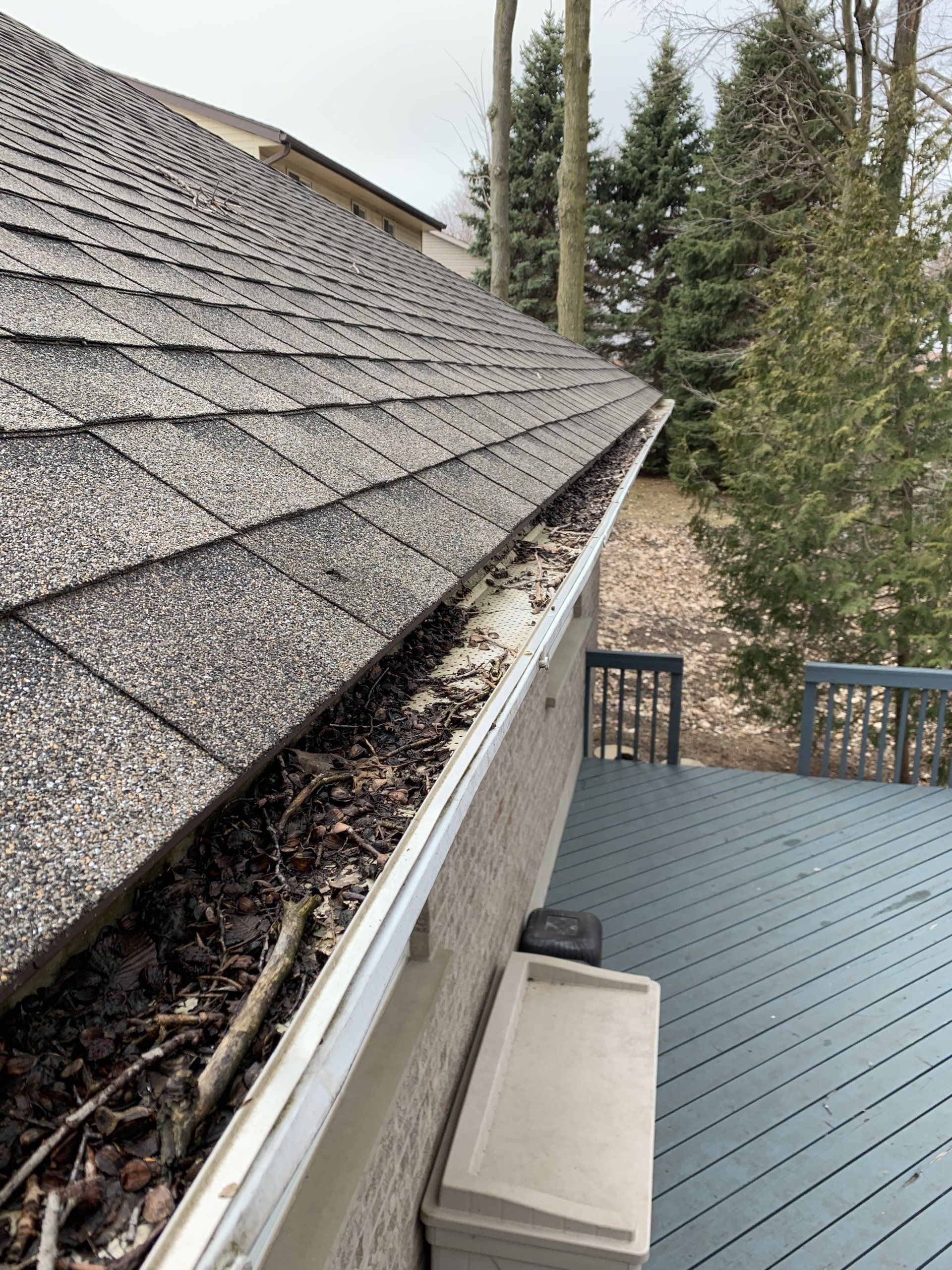 A gutter on the side of a house with a roof in the background.
