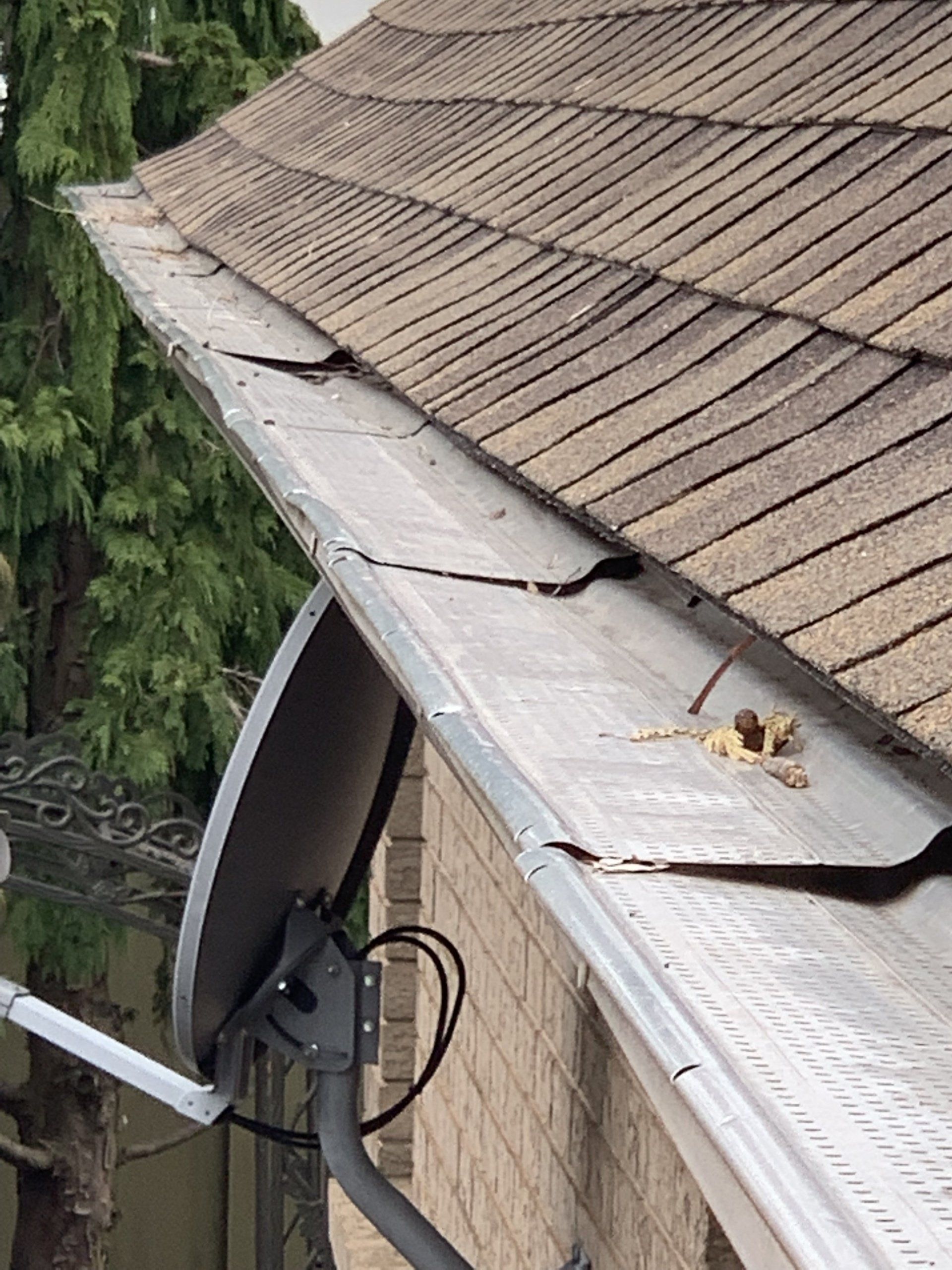 A satellite dish is sitting on the side of a house next to a gutter.