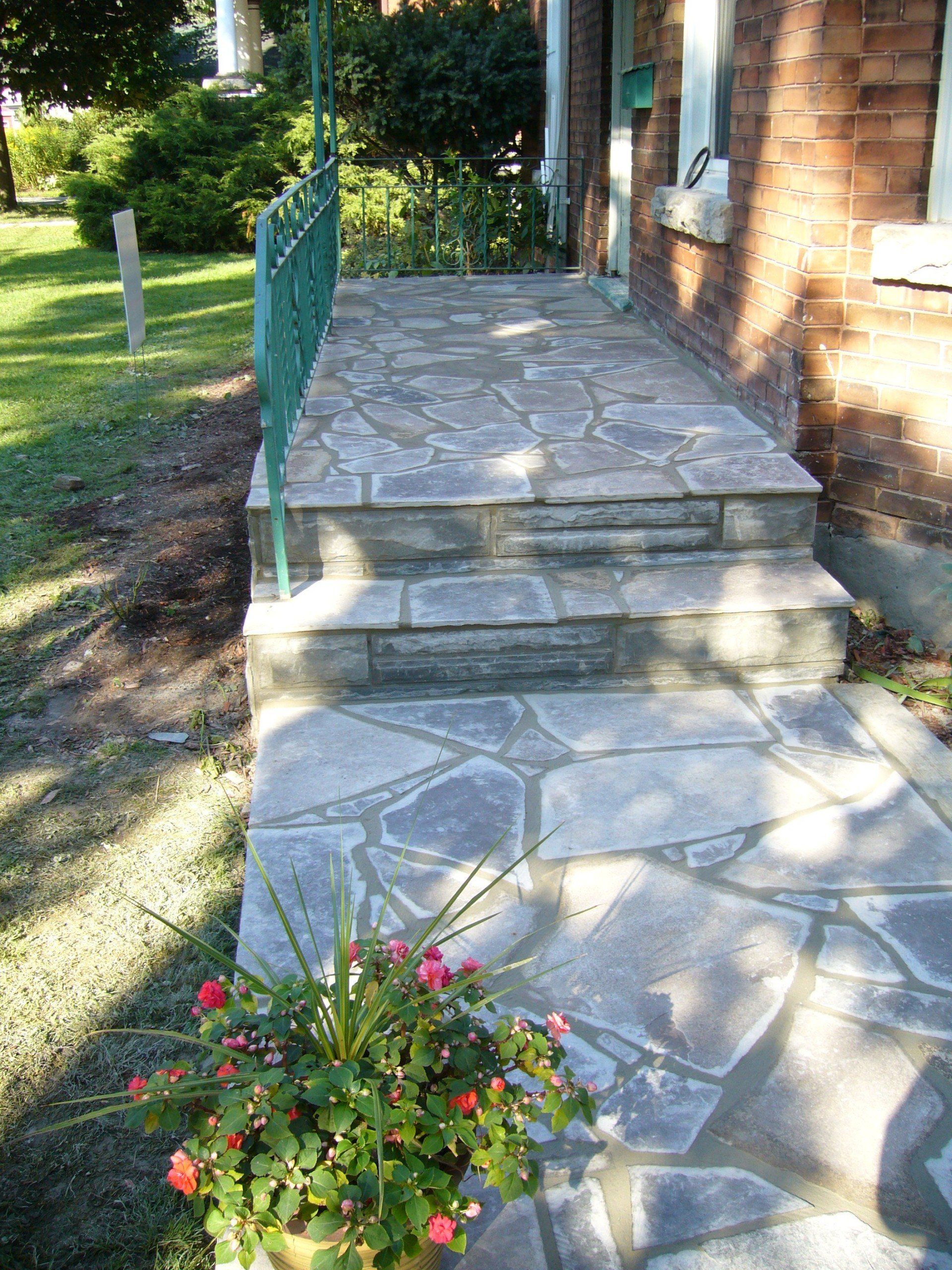 A stone walkway leading to a brick house with a potted plant in the foreground.