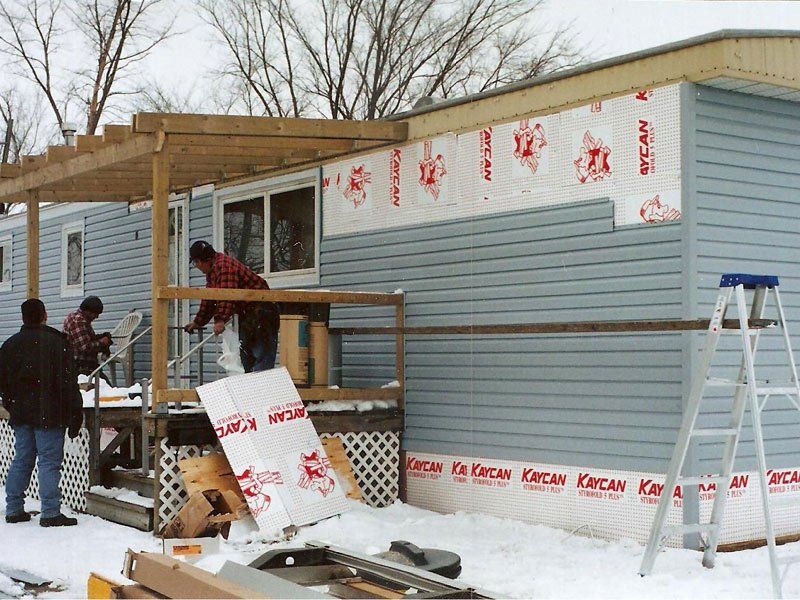A group of people are working on a mobile home with a ladder in the foreground