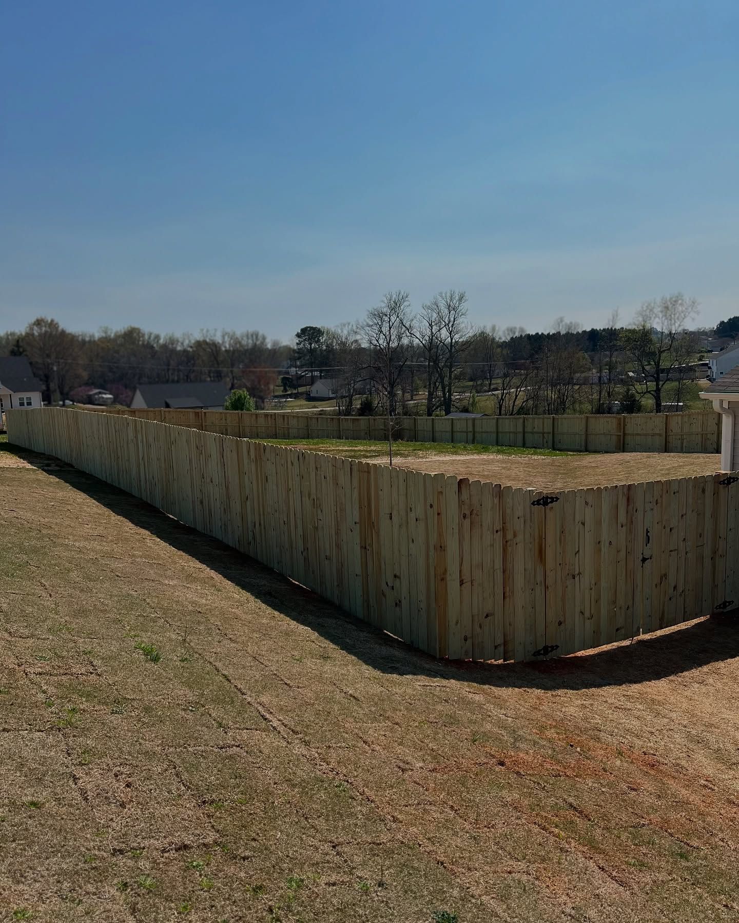 A long wooden fence surrounds a grassy field.