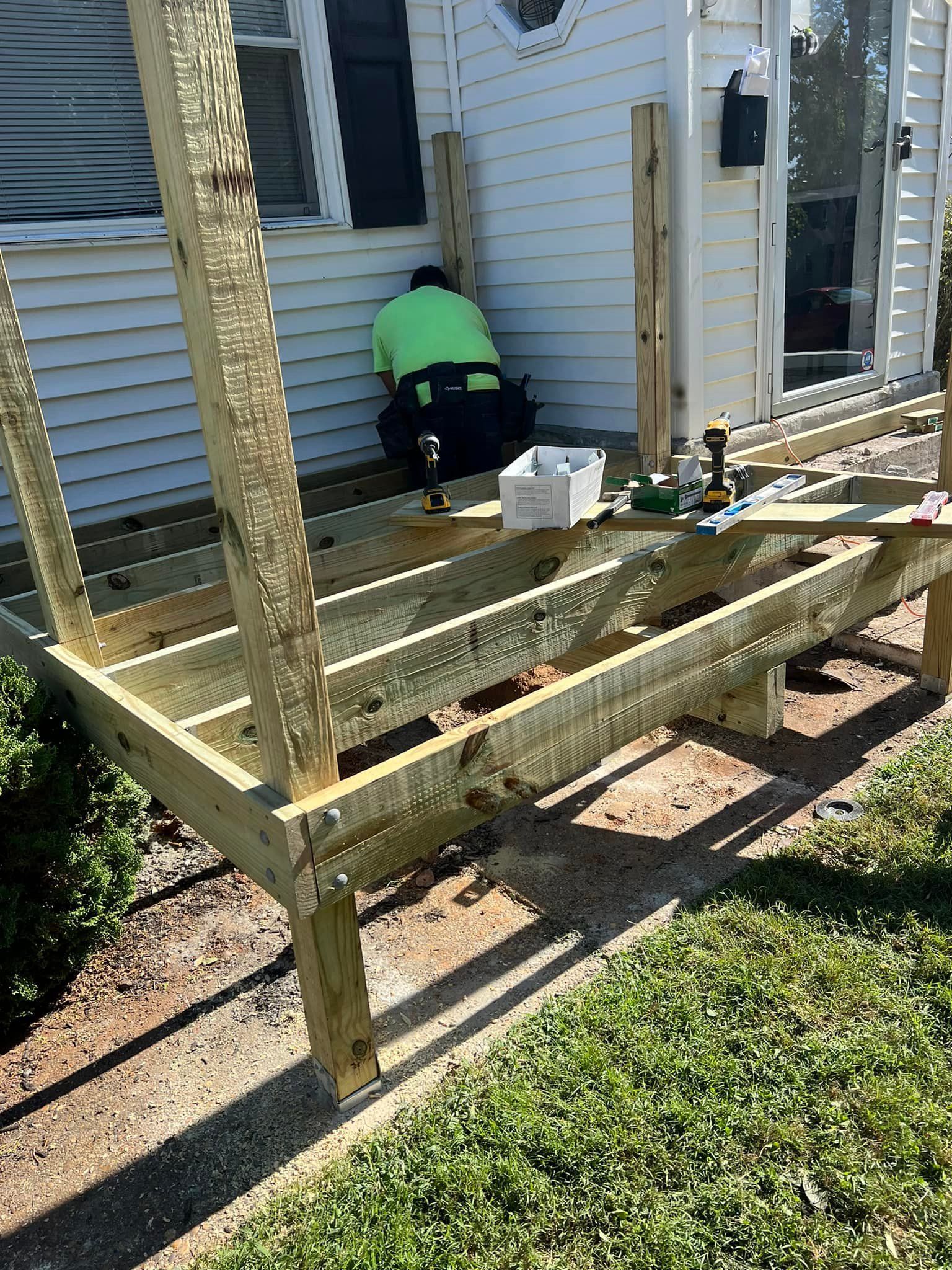 A man is working on a wooden deck in front of a house.