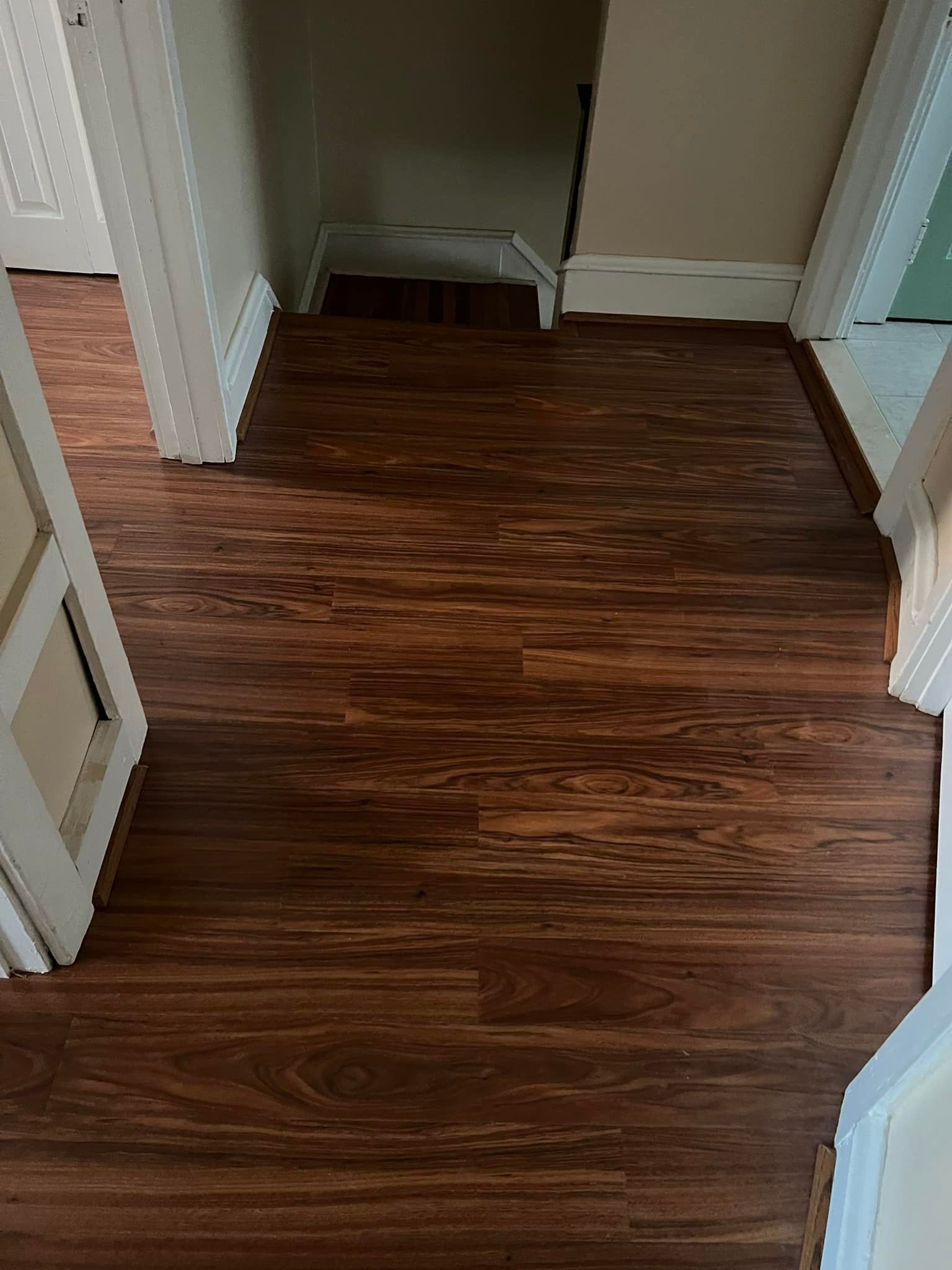 A hallway with a wooden floor and stairs leading up to the second floor.