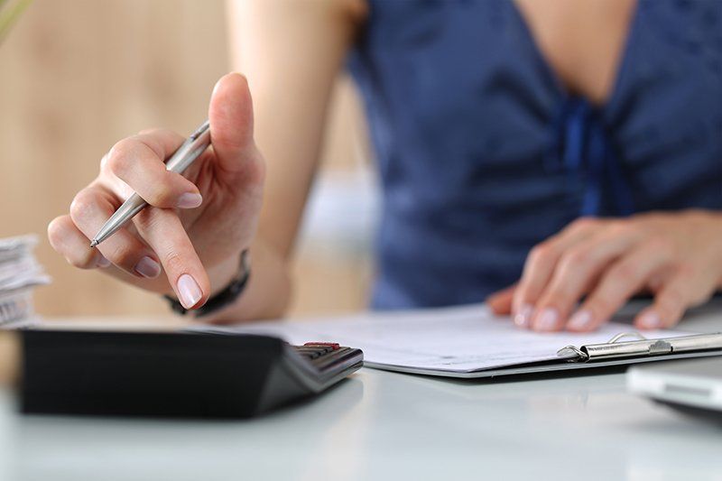 A woman is sitting at a desk using a calculator and a pen.