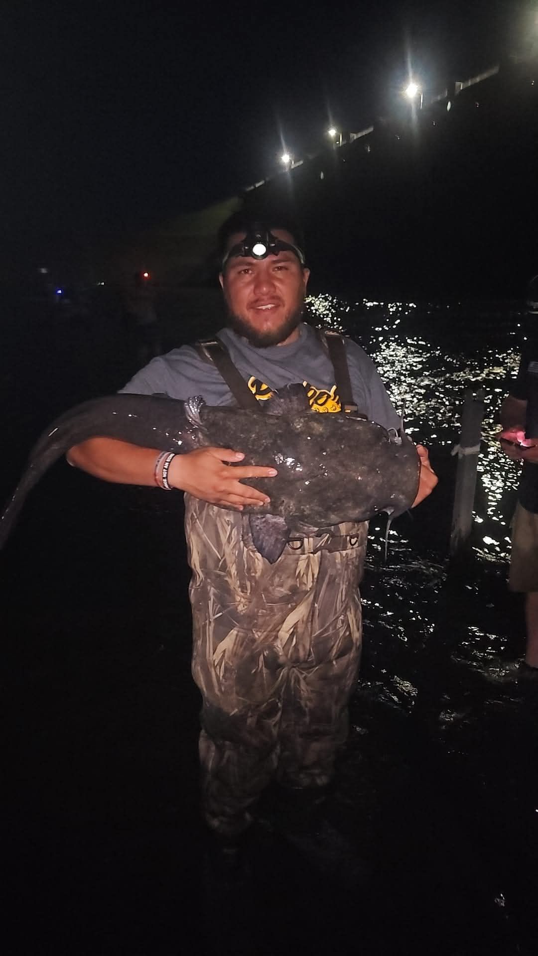 Mario Mendez holding a large fish in his hands in the water at night.