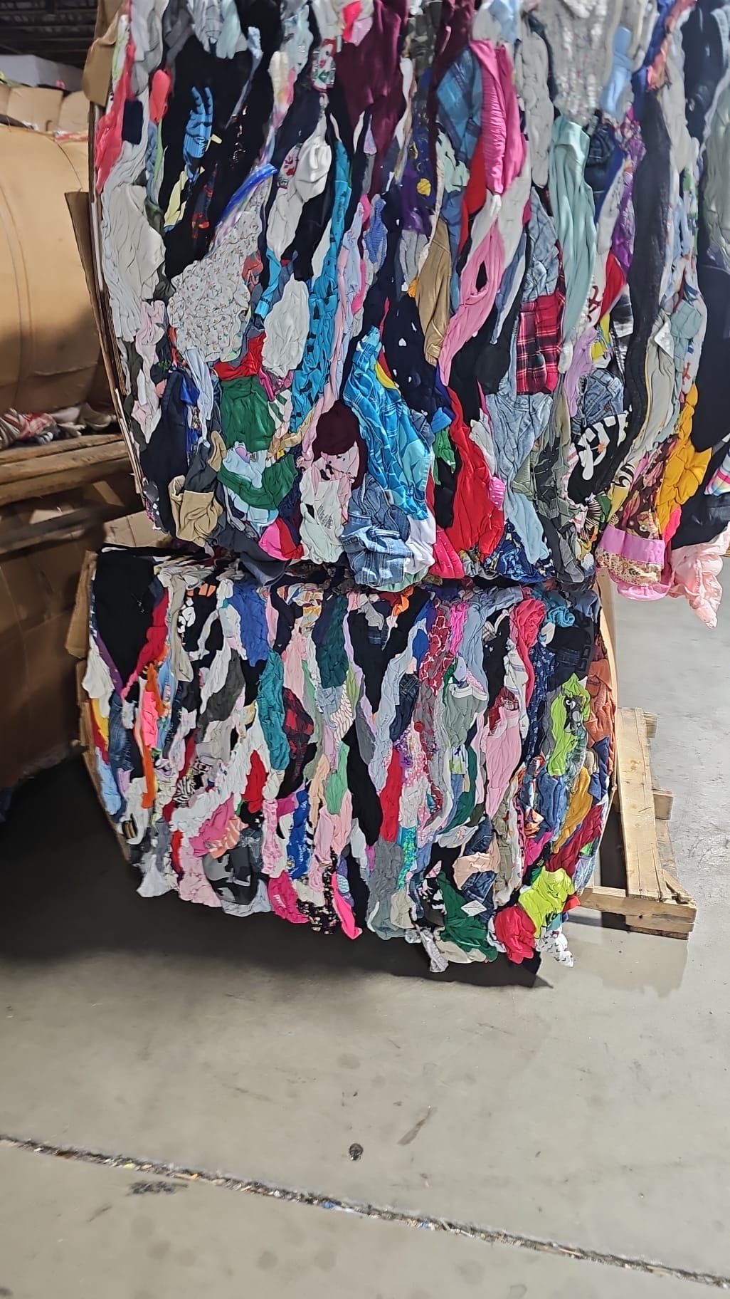 A large pile of colorful clothes is sitting on top of a wooden pallet.