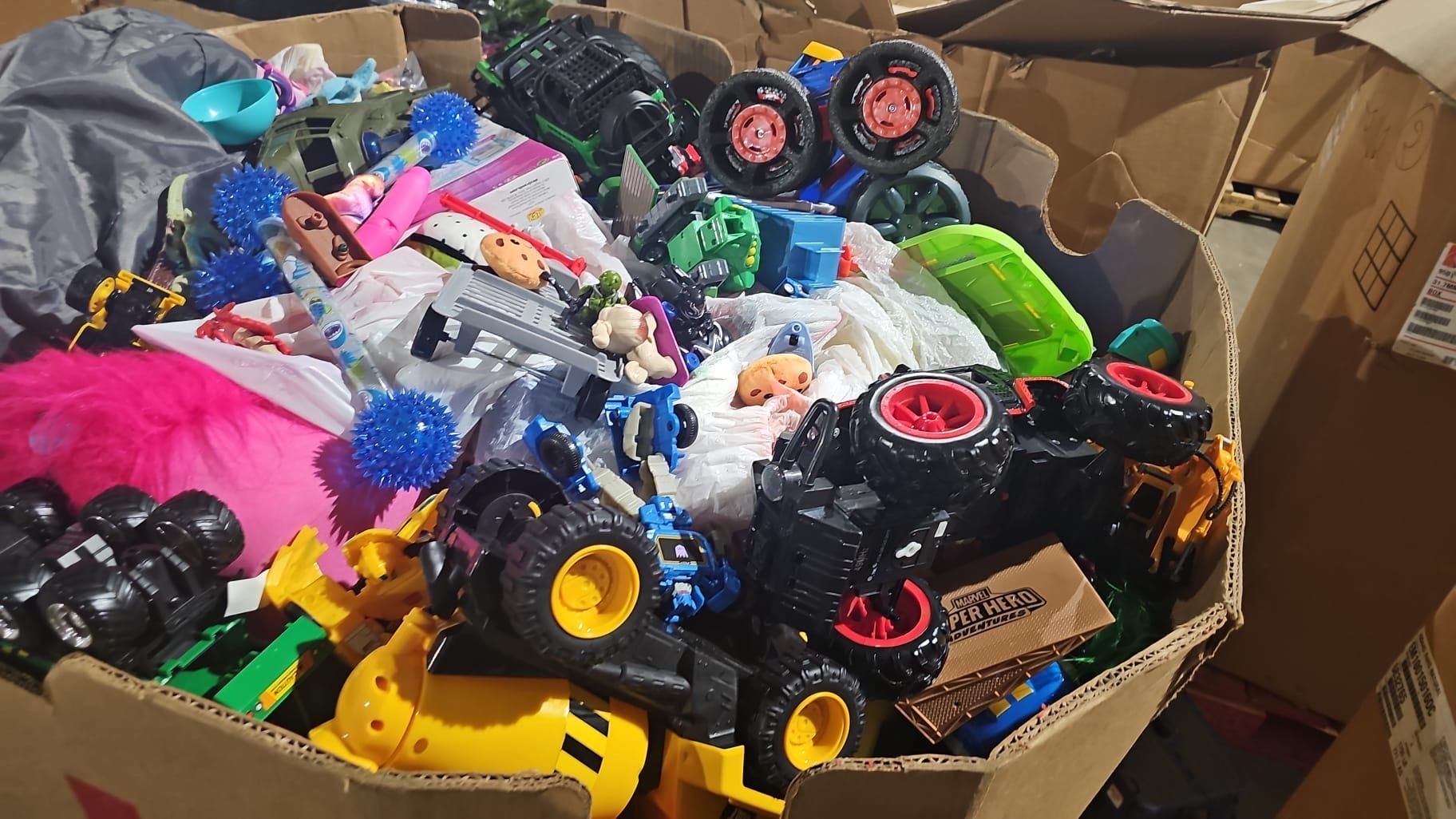 A cardboard box filled with lots of toys including monster trucks