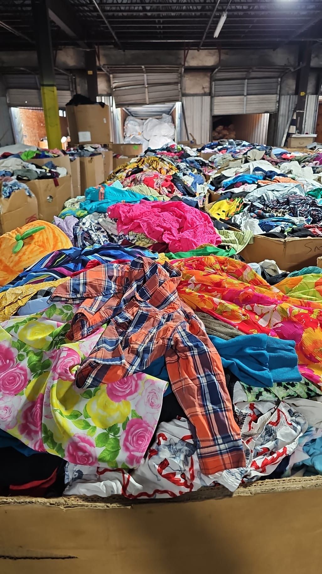 A pile of colorful clothes is sitting on top of a cardboard box in a warehouse.