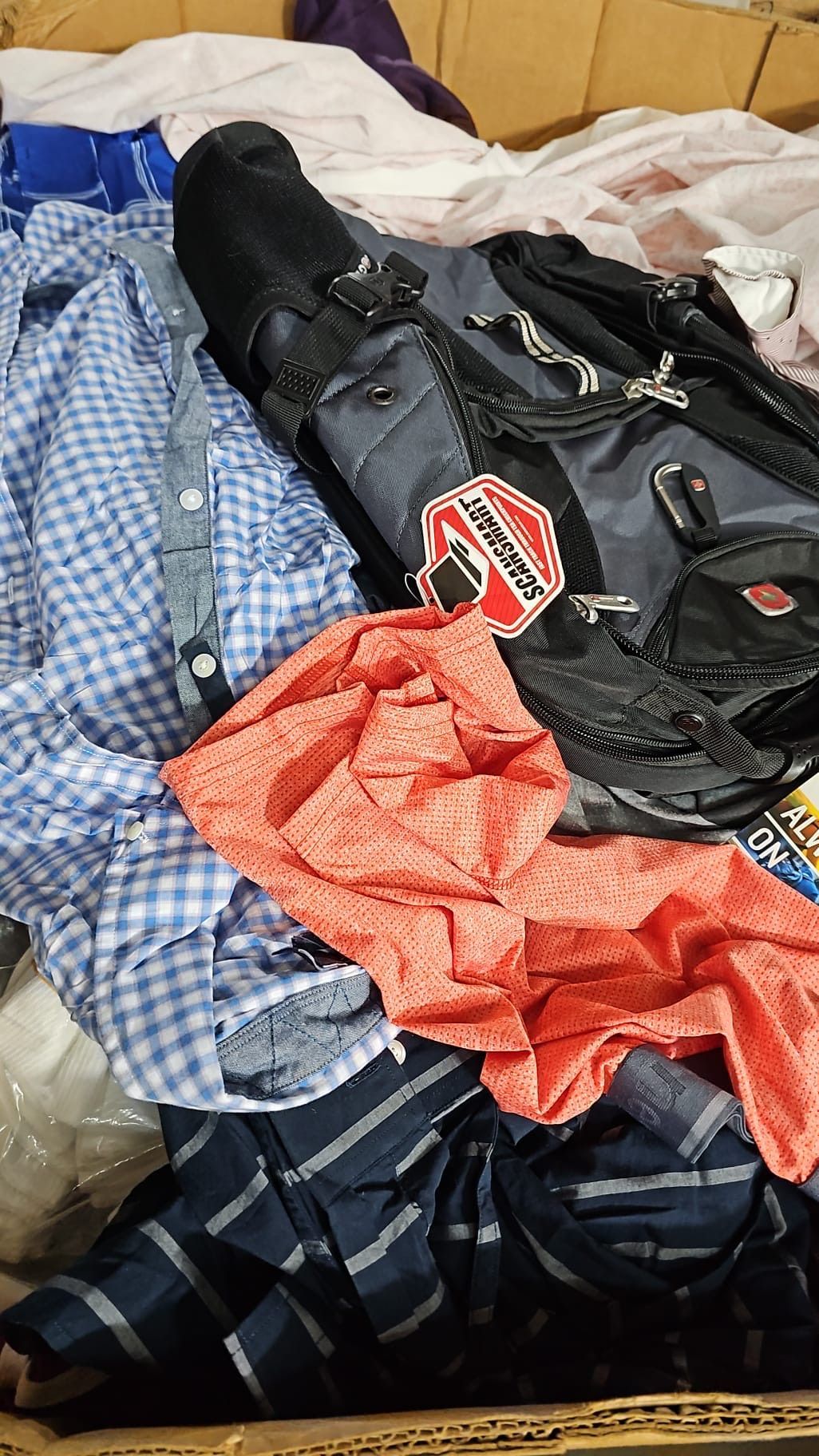 A pile of clothes and a backpack are in a box.