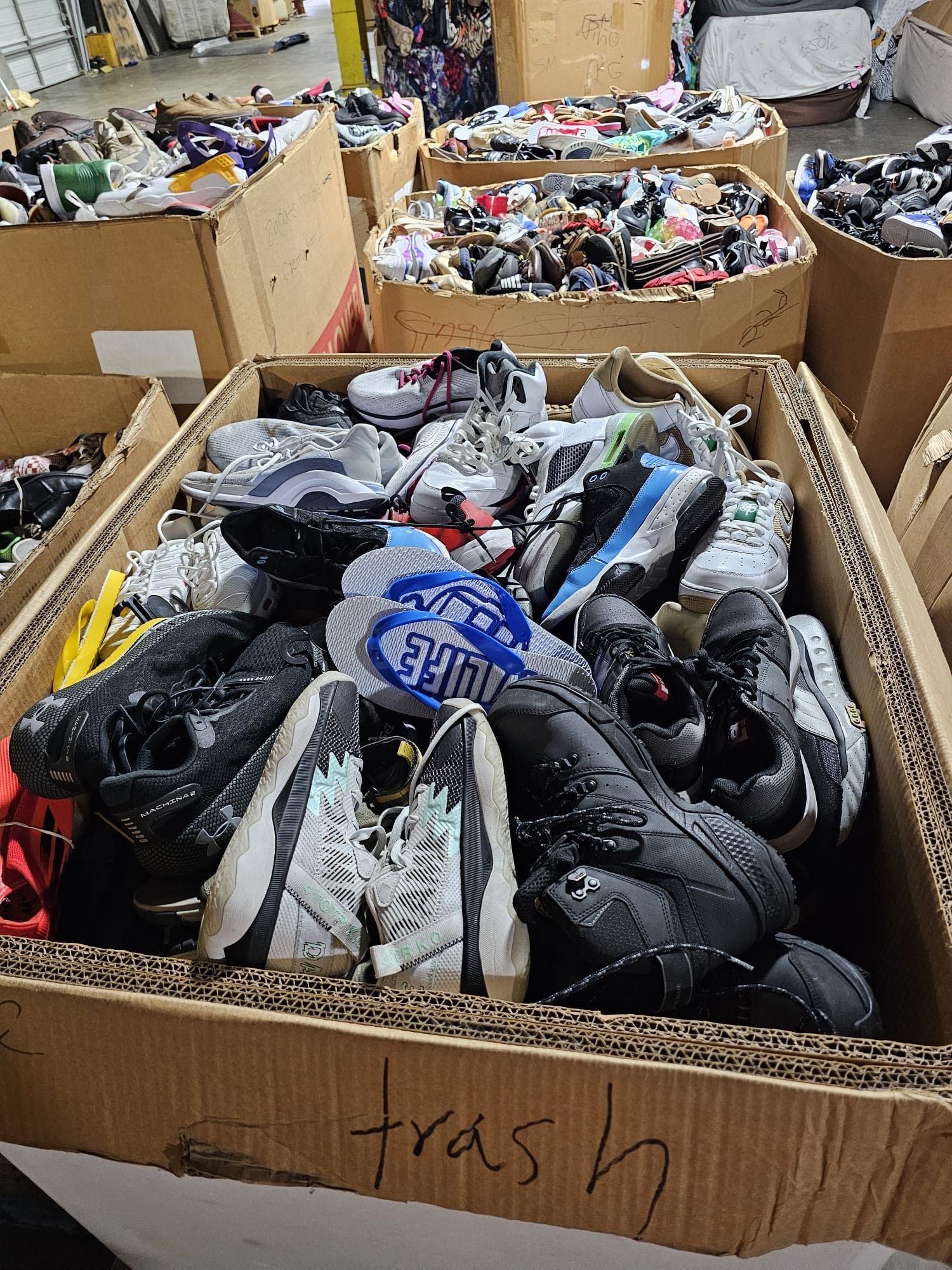 A pile of shoes in a cardboard box with the word trash written on it.
