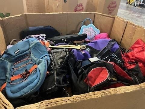 A cardboard box filled with lots of backpacks and handbags.