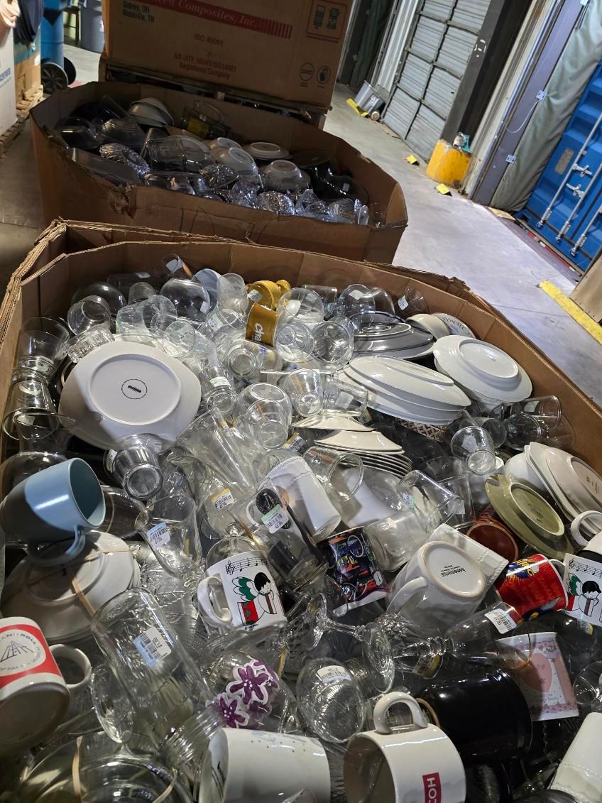 A cardboard box filled with lots of broken plates , cups , and glasses.