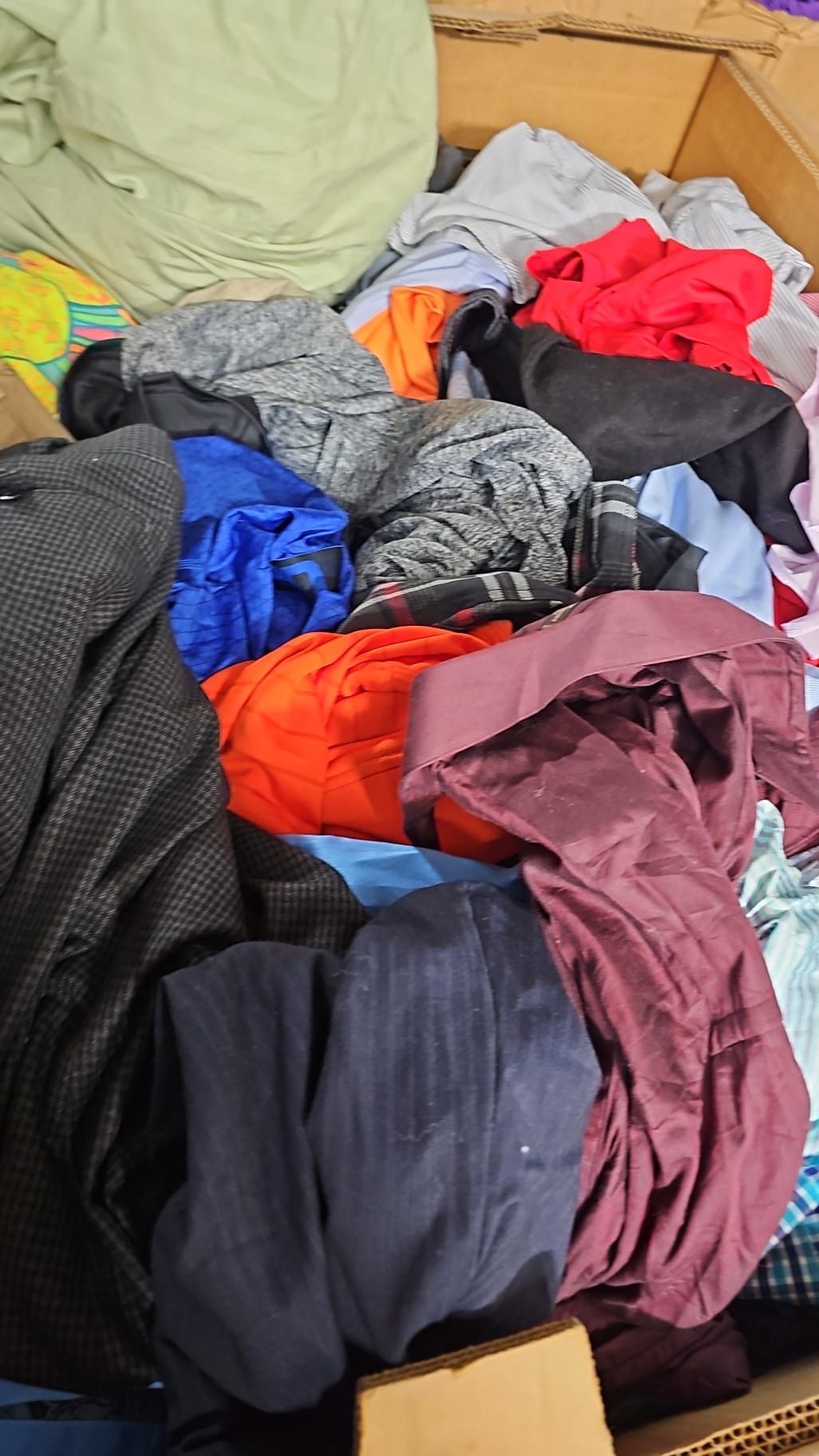 A cardboard box filled with lots of colorful clothes.