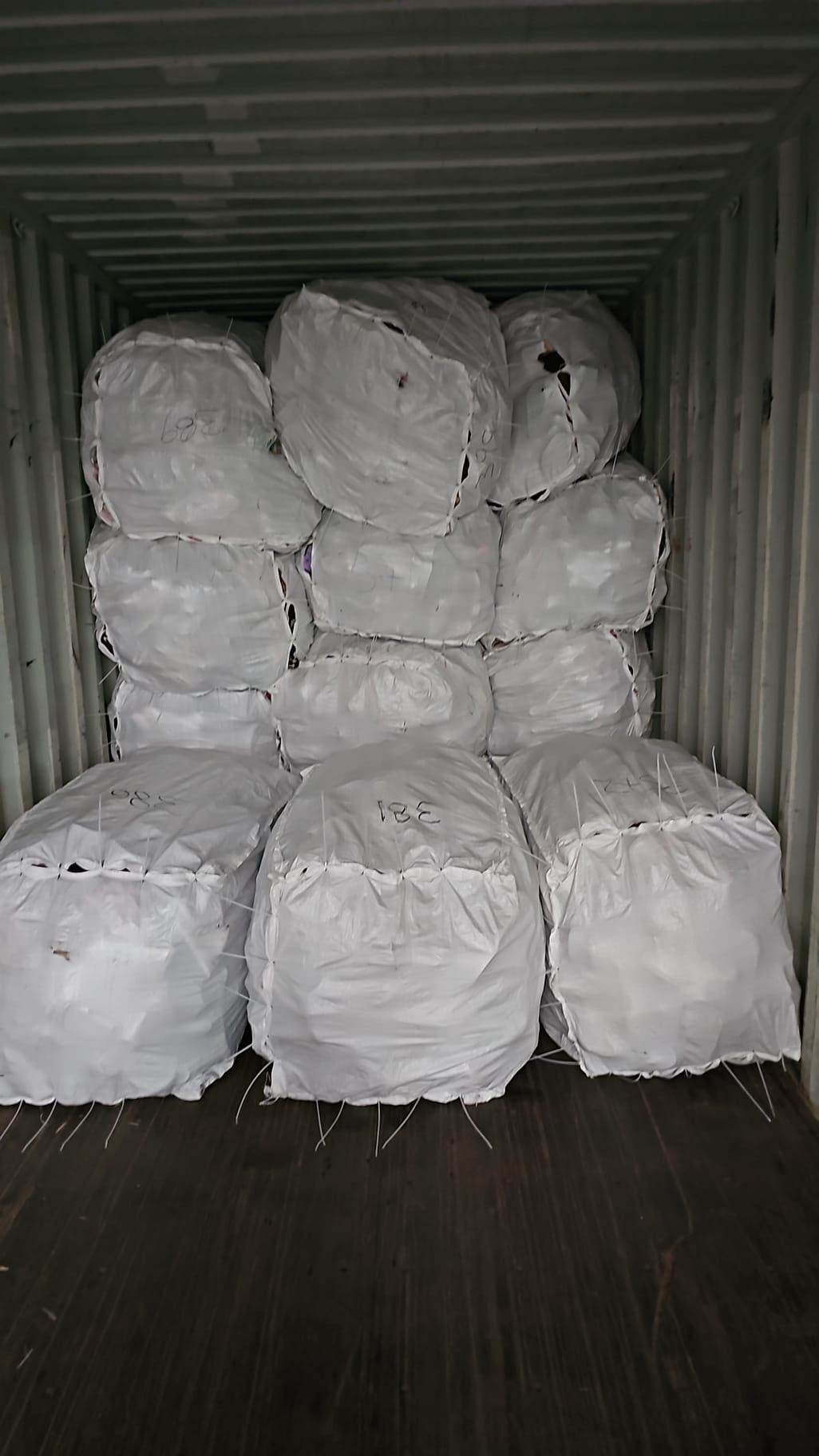A container filled with lots of white bags on a wooden floor.