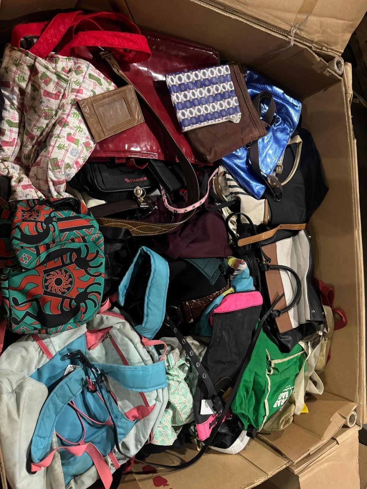A cardboard box filled with lots of handbags and backpacks.