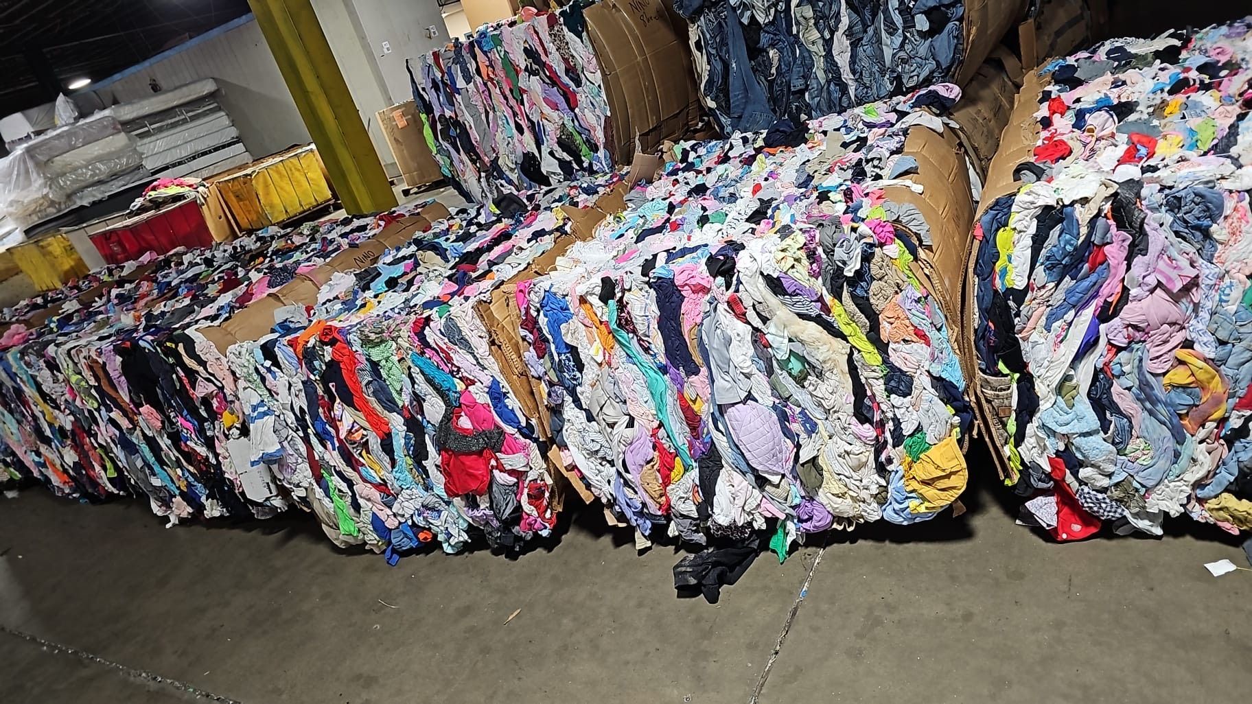 A bunch of colorful clothes are stacked on top of each other in a warehouse.