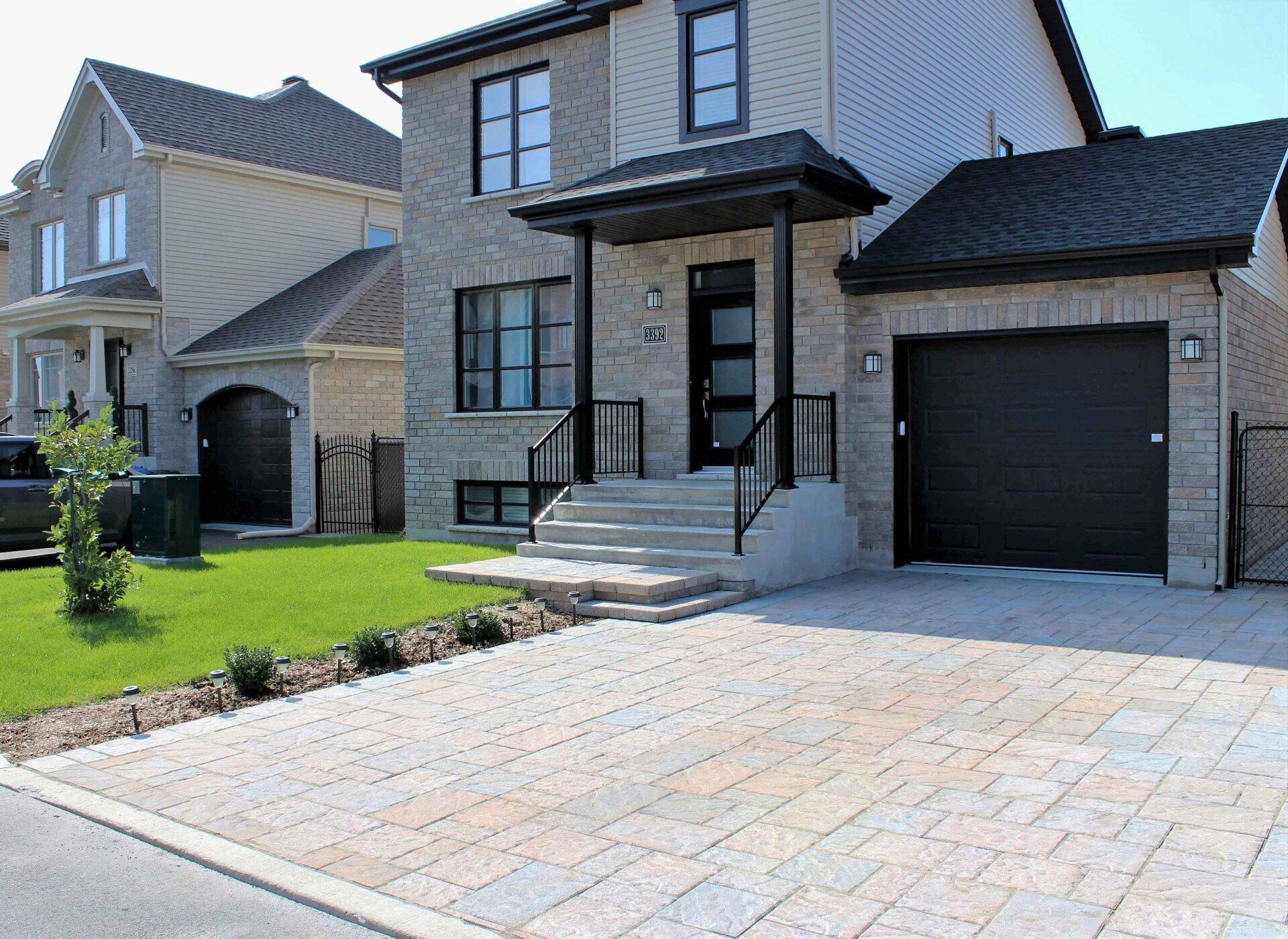 Une maison avec une porte de garage noire et une voiture noire garée devant.