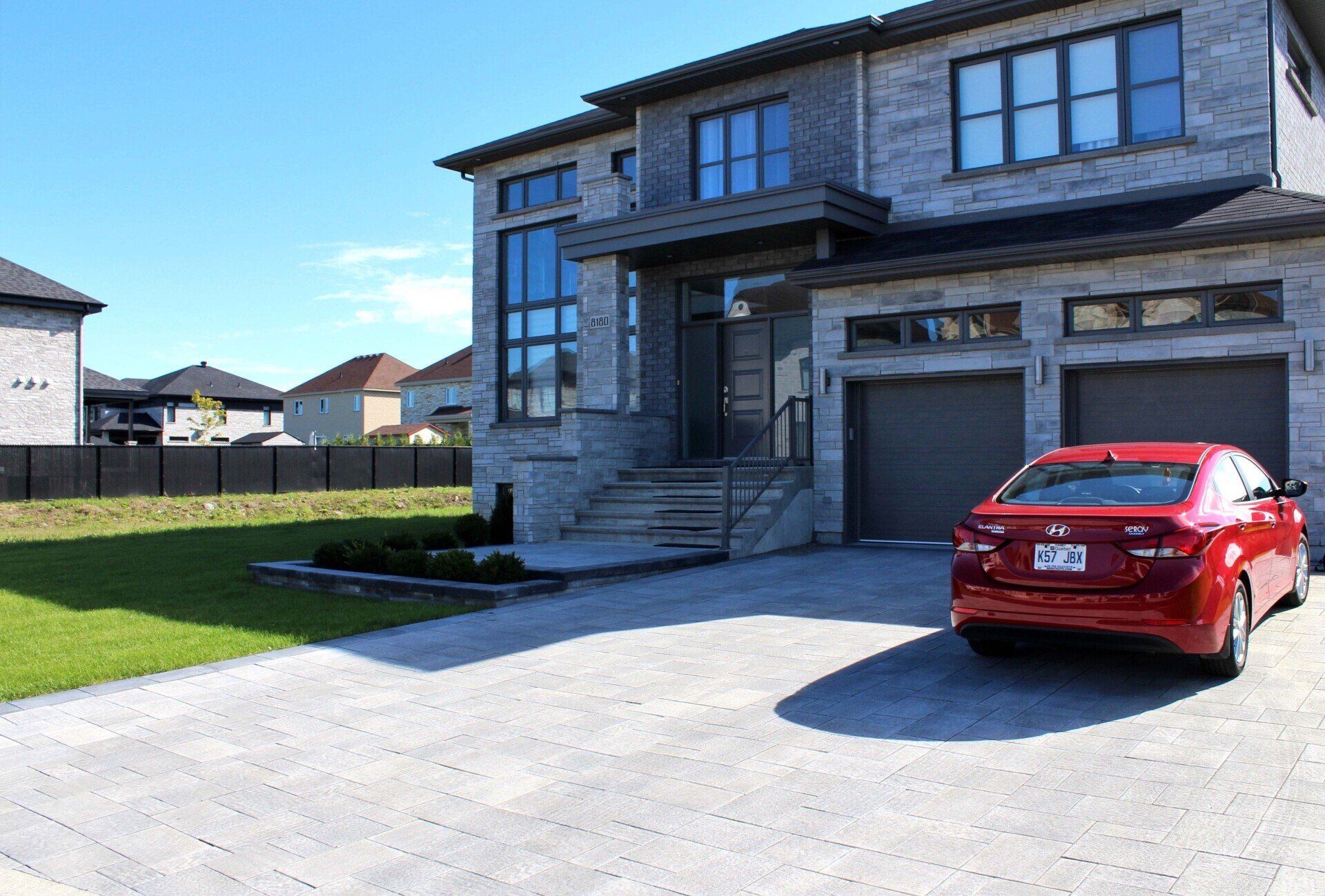 Une voiture rouge est garée devant une grande maison.