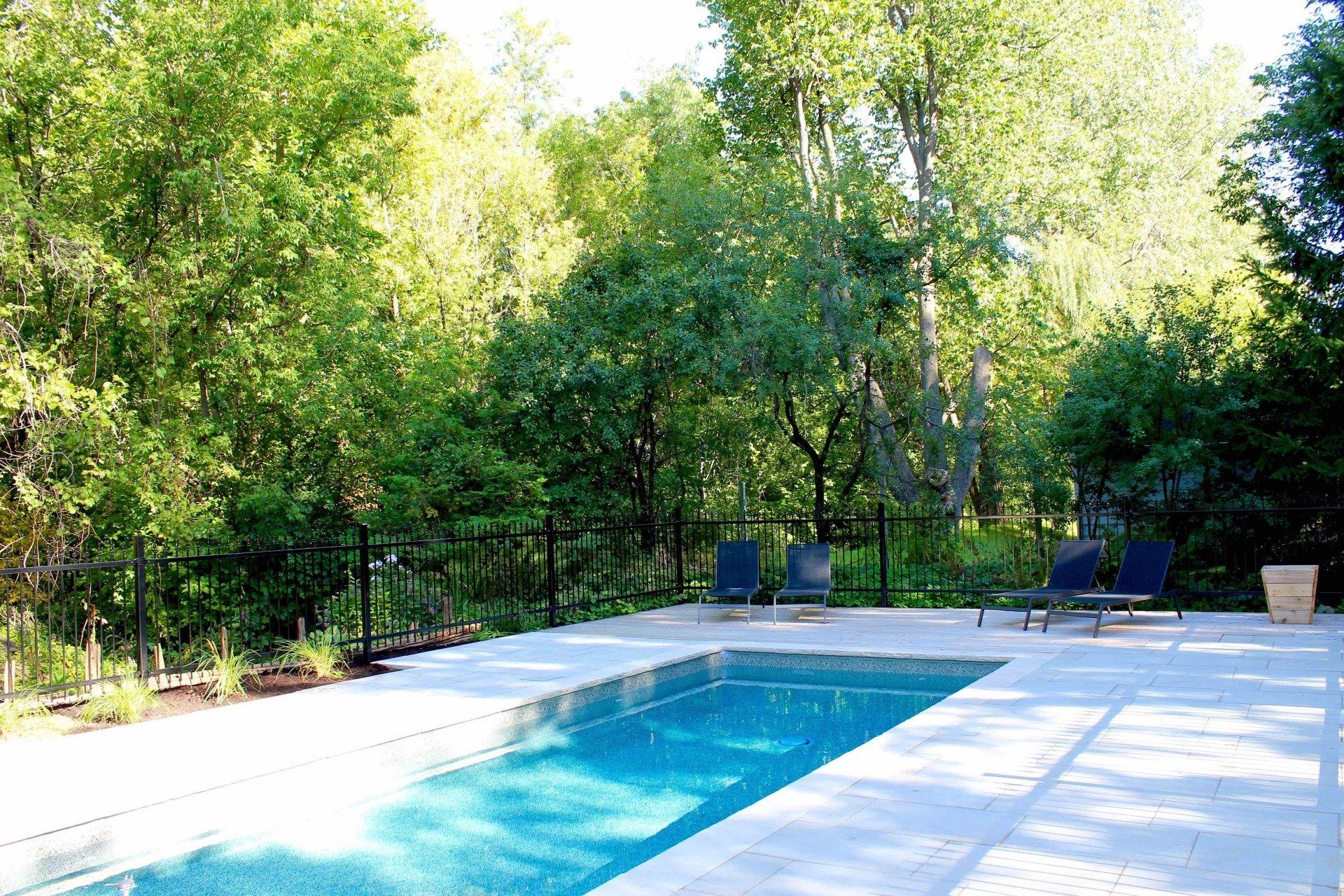 Une grande piscine est entourée d'arbres et de chaises.