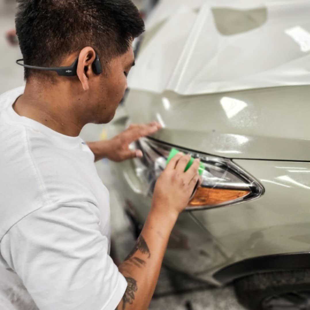 A person working on a car, cleaning a headlight. They wear a headset and have a tattoo.