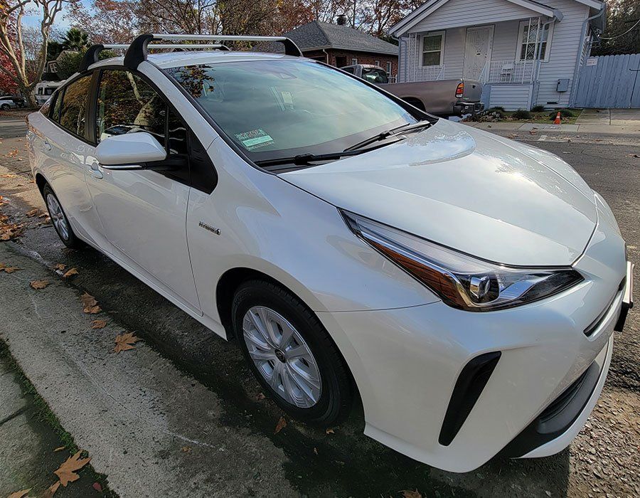 A white toyota prius is parked on the side of the road in front of a house.