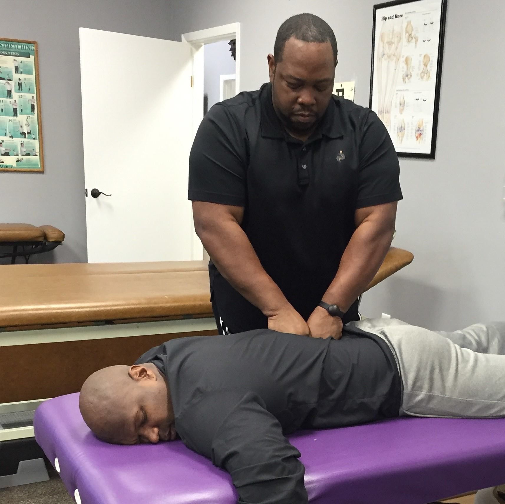 A man in a black shirt is giving a man a massage on a purple table