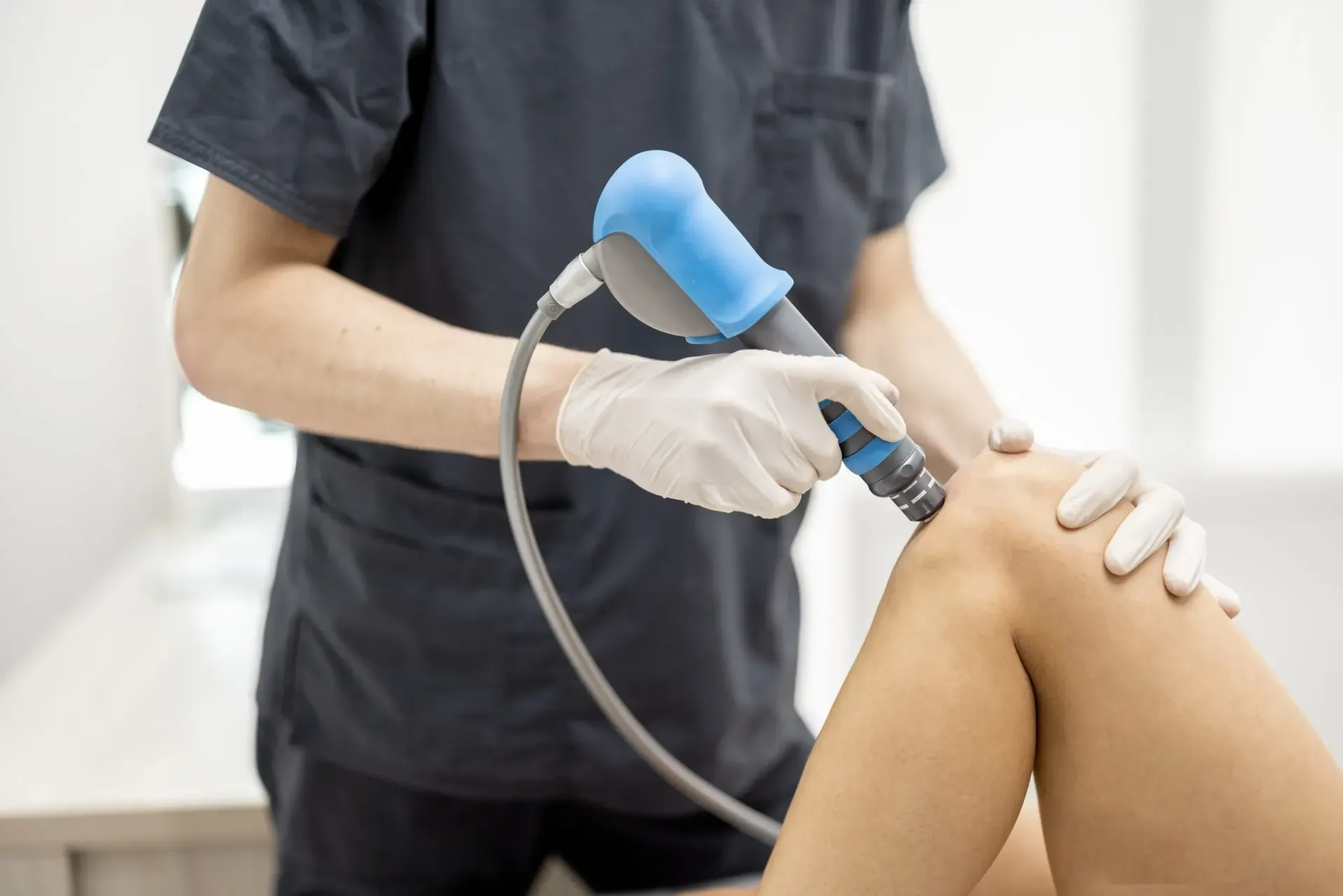 Person administering shockwave therapy to a patient's knee in a medical setting.
