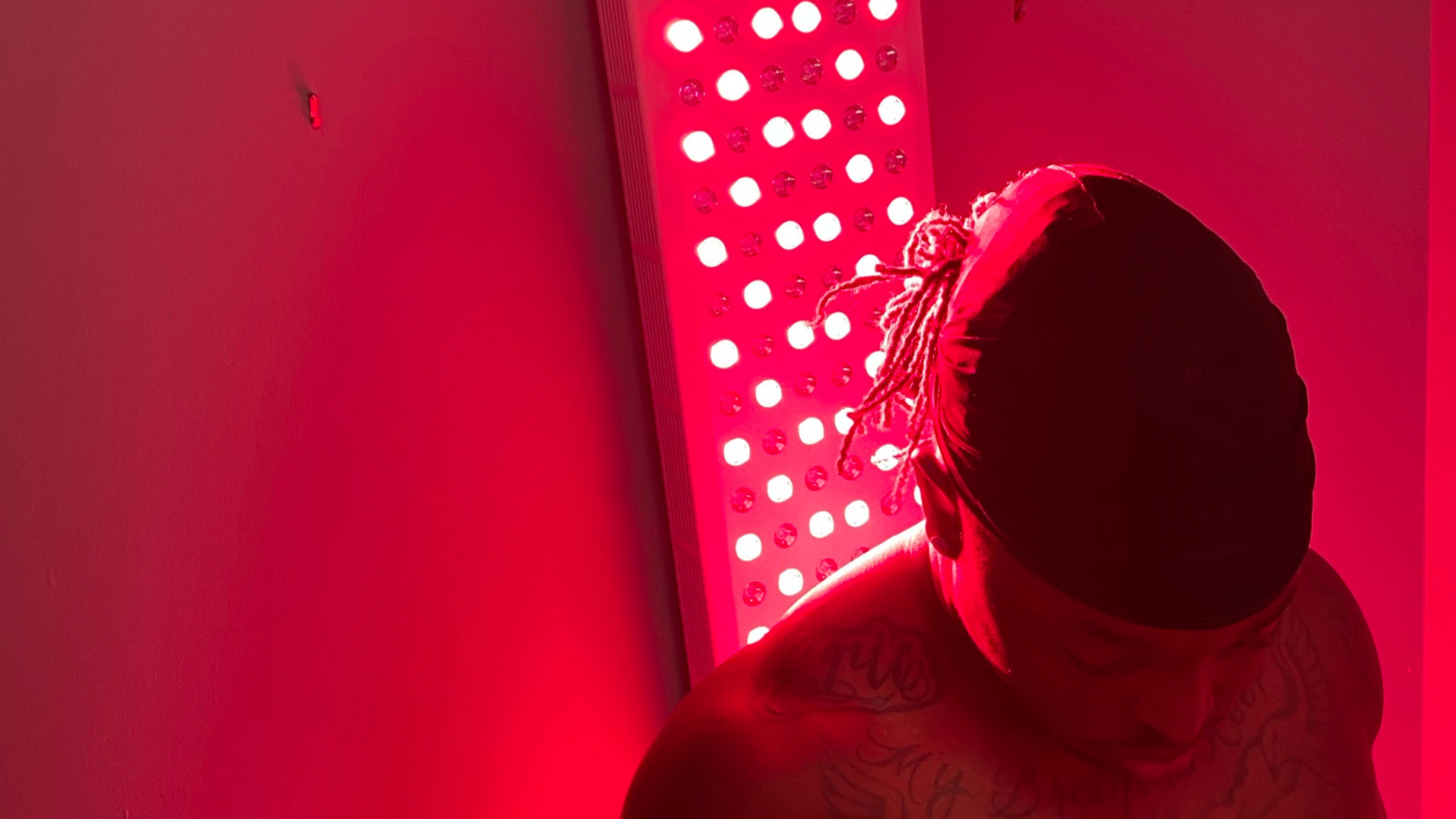 Person facing red light therapy panel; red light bathes them and the setting.