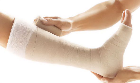 Person's leg in a cast being wrapped with bandage by another person's hands, isolated on white background.