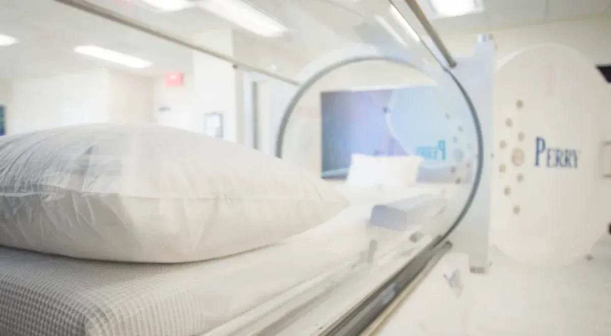 A white bed with a pillow inside a clear hyperbaric chamber.