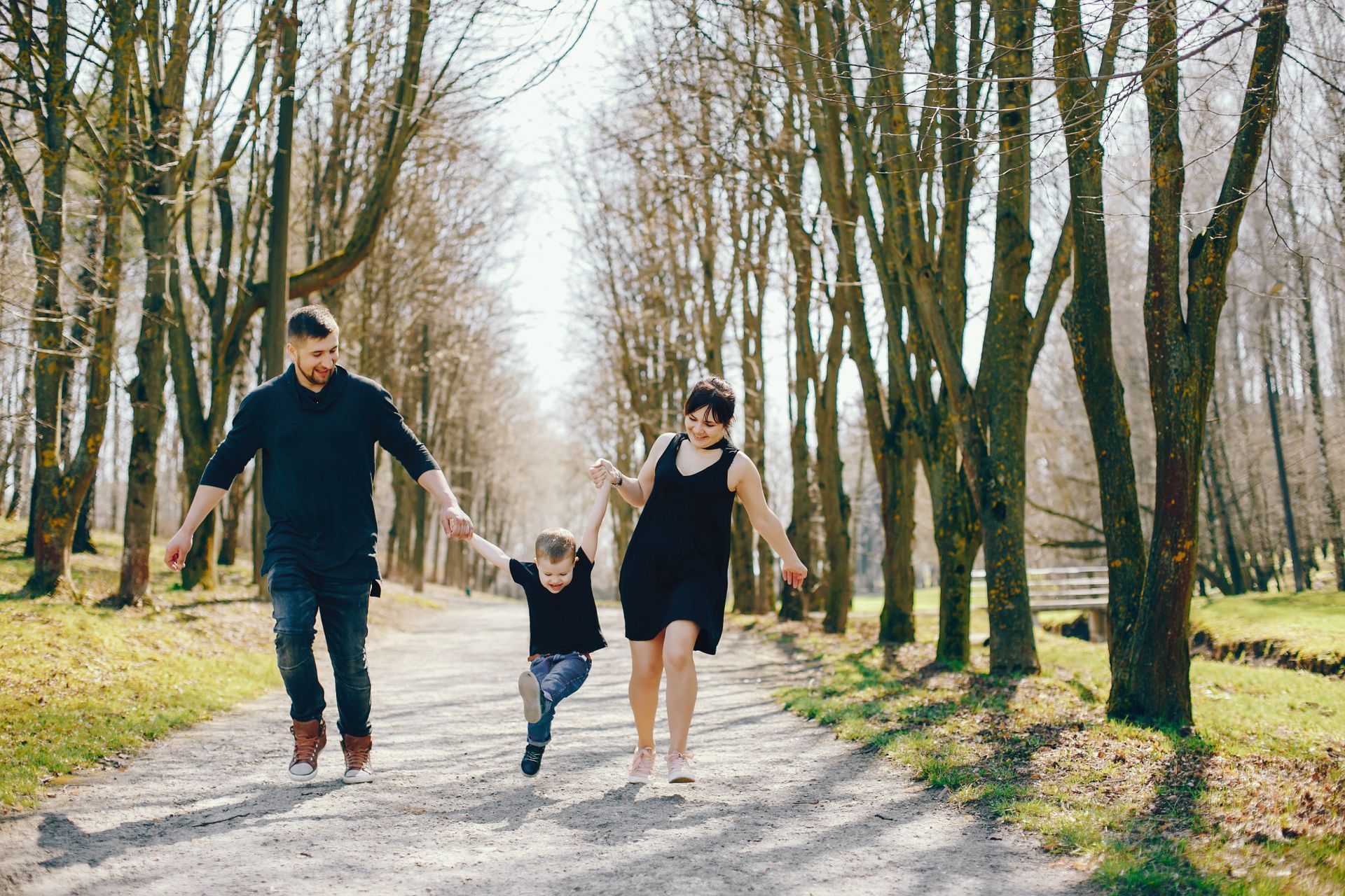 Family holding hands walking on a path in a park with trees, sunny day.