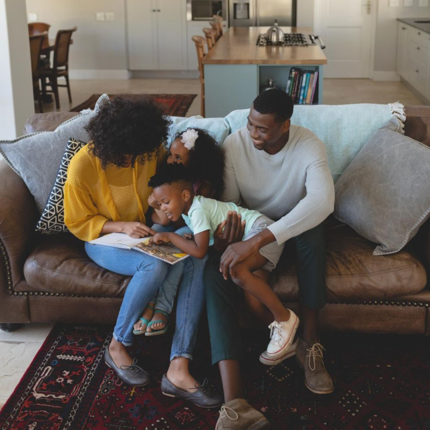 Family sitting on a brown couch reading a book together in a living room.