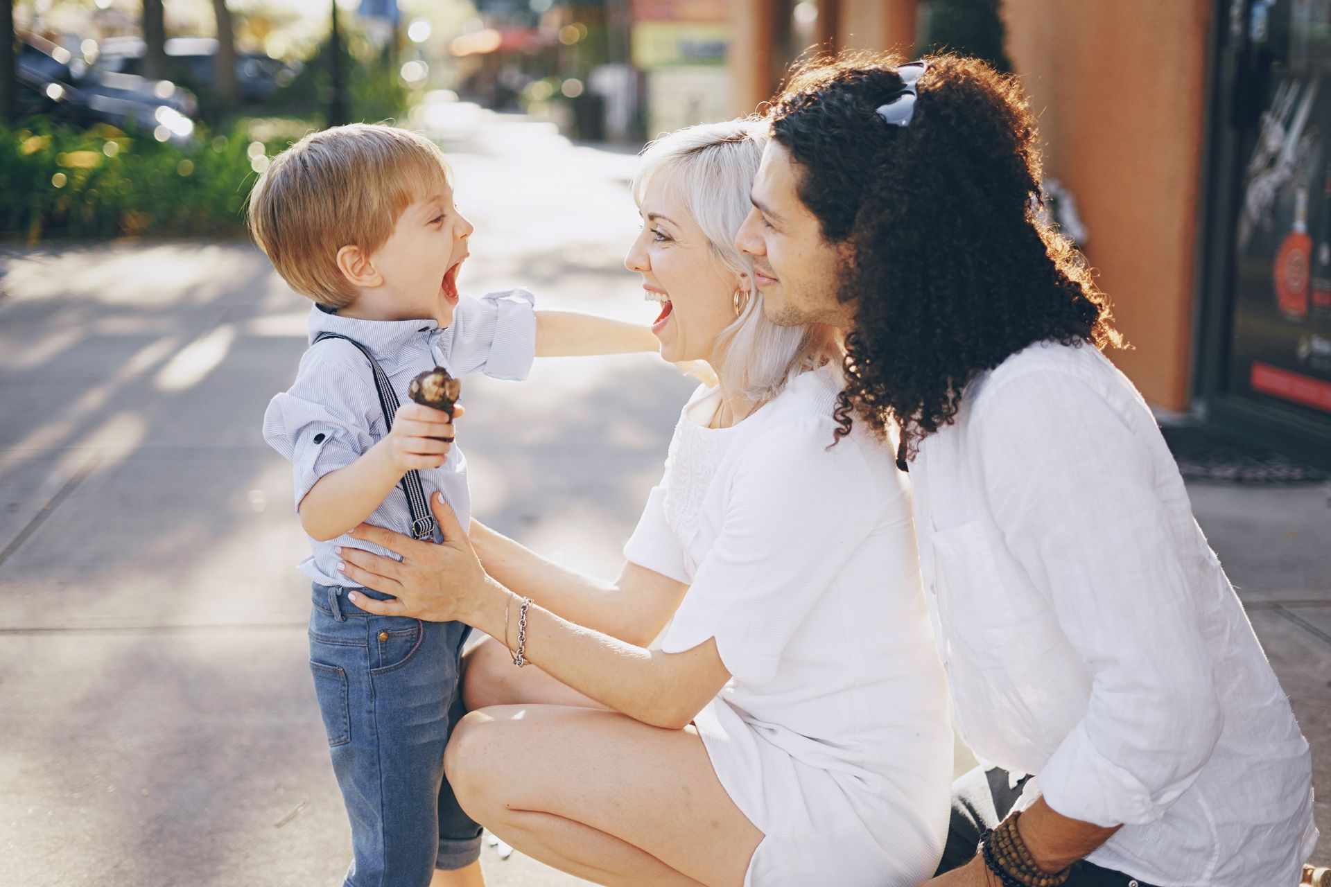 Child laughing, holding ice cream, with two adults, outdoors, sunny.
