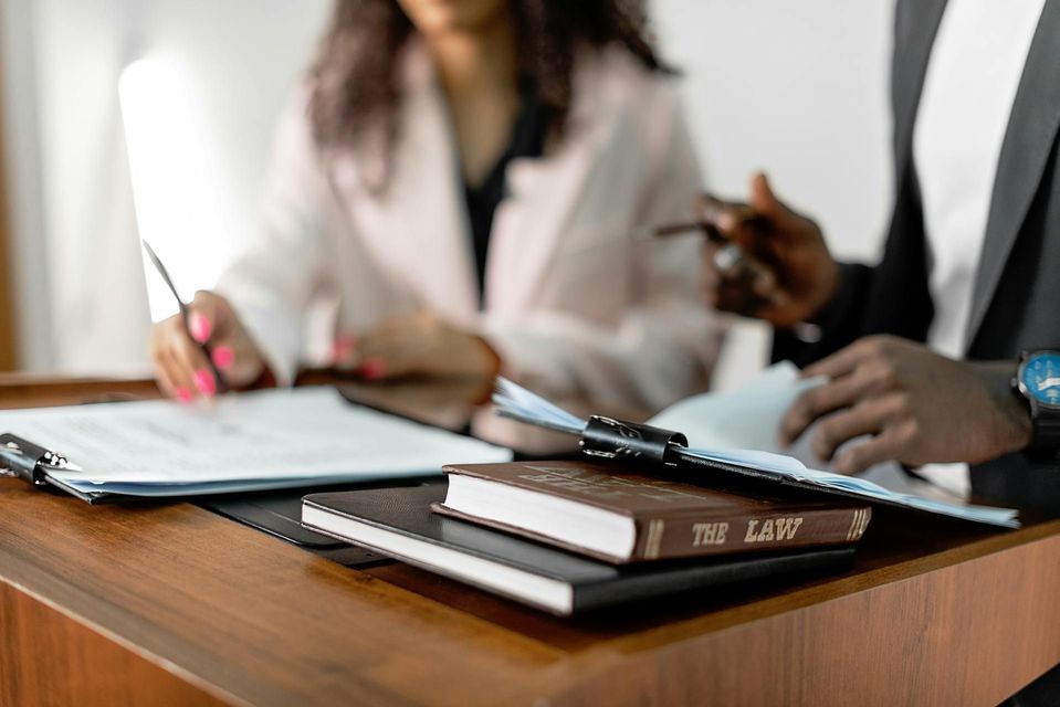 Two people reviewing documents, one writing. A book labeled 